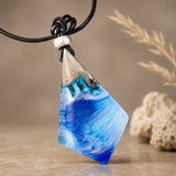 WAVE WHISPER – handgefertigter Holz-Harz-Anhänger aus Maserholz und blau-weißem Epoxidharz, maritimer Naturschmuck am schwarzen Lederband, clean inszeniert mit dezenter Stranddeko
