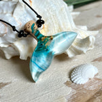 Walflossen-Anhänger „Flossenklang“ – handgefertigtes Unikat aus Maserholz und blau-weißem Harz. Die elegant geschwungene Form erinnert an die Flosse eines Wals und symbolisiert Freiheit, Stärke und Naturverbundenheit. Mit verstellbarem schwarzen Lederband und Onyxperlen gefertigt, ist jedes Stück ein individuelles Schmuckstück für Meeresliebhaber und Natursuchende. Maritimer Halsschmuck, inspiriert vom Ozean, glatt poliert und mit Liebe zum Detail von Hand gearbeitet.