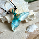 Walflossen-Anhänger „Flossenklang“ – handgefertigtes Unikat aus Maserholz und blau-weißem Harz. Die elegant geschwungene Form erinnert an die Flosse eines Wals und symbolisiert Freiheit, Stärke und Naturverbundenheit. Mit verstellbarem schwarzen Lederband und Onyxperlen gefertigt, ist jedes Stück ein individuelles Schmuckstück für Meeresliebhaber und Natursuchende. Maritimer Halsschmuck, inspiriert vom Ozean, glatt poliert und mit Liebe zum Detail von Hand gearbeitet.