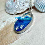 „Riffschatz“ – ovaler Harz-Anhänger mit plastischer 3D-Welle in Blau/Türkis, weißer Schaumkrone und Muschel-/Korallen-Stickern am Grund. Die Sticker sind unter klarem Harz versiegelt. Silber-Legierung, ca. 3,9 × 2,3 cm, an einer ca. 56 cm langen versilberten Kette. Handgefertigt, hochglänzend, jedes Stück ein Unikat.