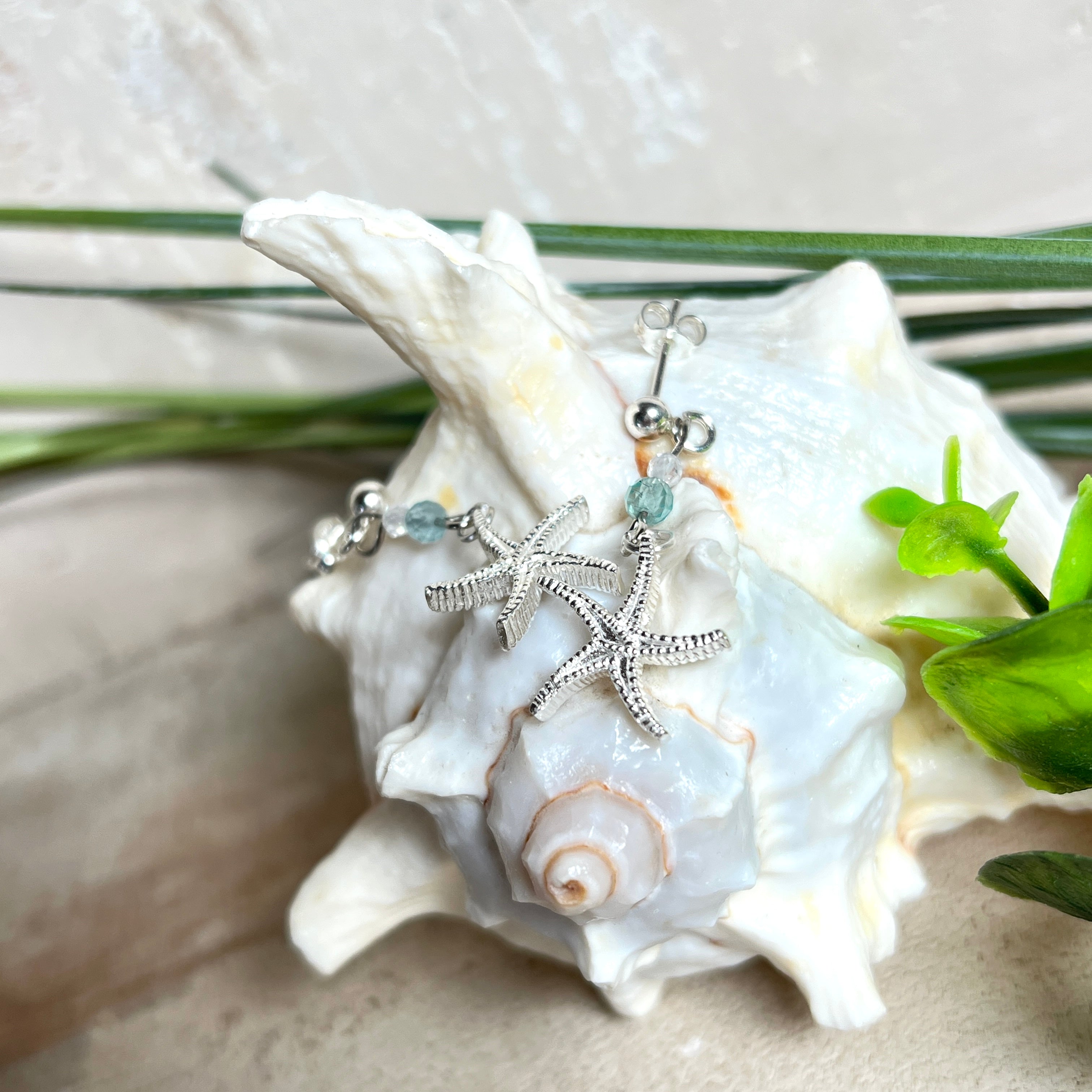 Edle „Ocean Star“ Ohrringe aus 925 Sterling Silber mit Seestern-Anhängern (18 × 17 mm), verziert mit einer aquablauen Apatitperle und funkelndem Zirkonia. Länge getragen: 45 mm. Maritime Schmuckstücke, die das Funkeln des Meeres einfangen – elegant, hochwertig und ein ideales Geschenk für Meeresliebhaber und Sommerträume.