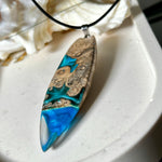 Handgefertigter Surfbrett-Anhänger aus Maserholz und transparentem Harz mit Farbverlauf in Blau und Weiß. Die natürliche Maserung des Holzes trifft auf ozeanartige Harzstrukturen. Größe ca. 6,7 x 2 cm, mit Edelstahlöse und Lederband inkl. Karabinerverschluss (45 cm + 5 cm Verlängerung). Jedes Stück ist ein Unikat – maritim, modern und mit viel Liebe gefertigt.
