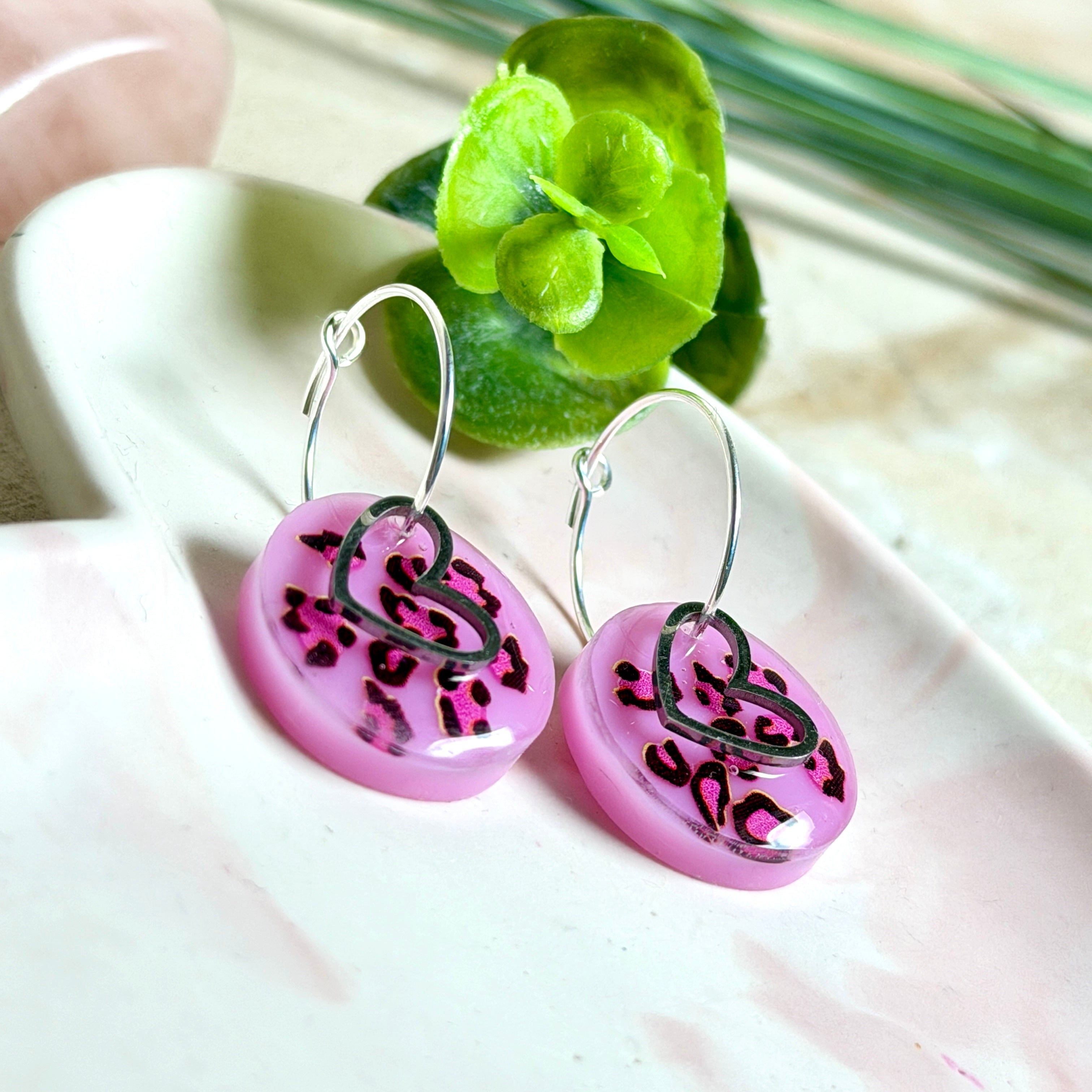 Handgemachte Leo-Creolen aus 925 Silber: Silber-Creolen 16 mm mit rosa Harz-Scheibe (2 cm) im Leoparden-Look und Edelstahl-Herzanhänger. Hängende Ohrringe in Animal-Print Stil, Gesamtlänge ca. 3,5 cm. Resin-Ohrringe für Alltag, Party oder Festival, femininer Statement-Schmuck in Rosa/Pink mit silberfarbenen Metallteilen. Einzeln gegossen, jedes Paar ein Unikat; leichte Abweichungen im Muster, Farbspiel und kleine Luftbläschen sind möglich und typisch für Handarbeit.