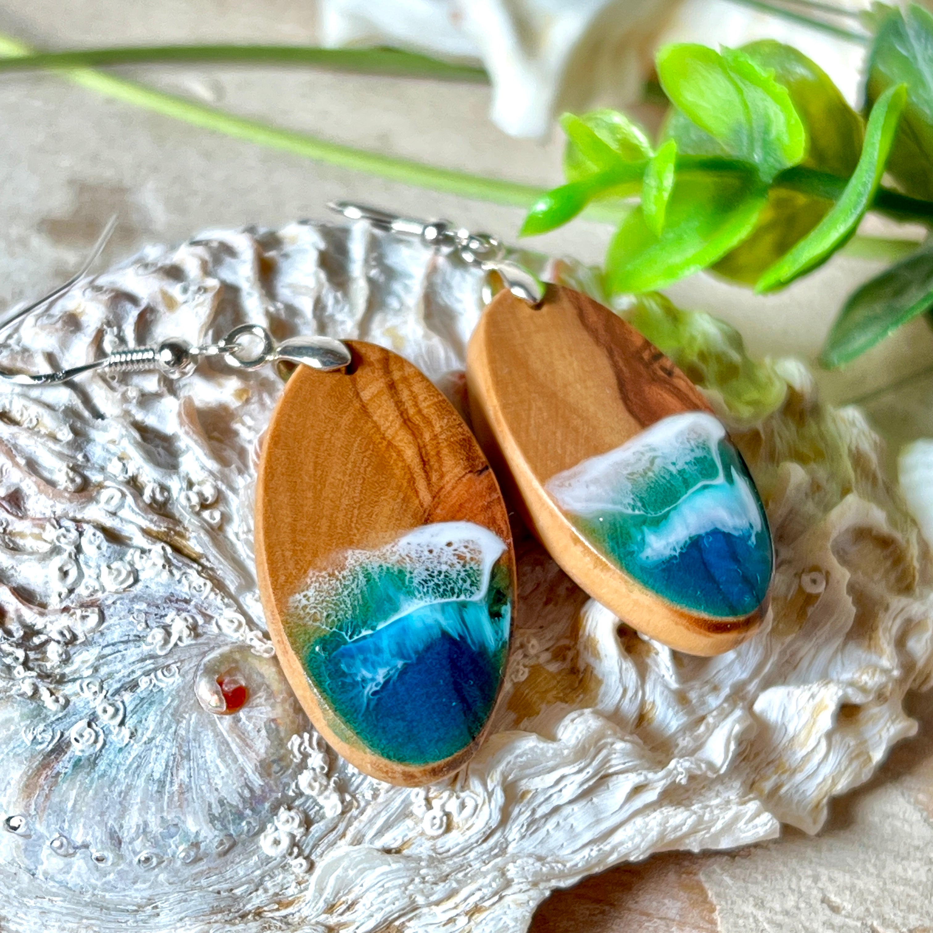Handgefertigte Ohrringe „Wave Harmony“ aus Olivenholz und Epoxidharz in Blau-, Türkis- und Weißtönen. Das Design erinnert an Meereswellen am Strand. Jeder Ohrring ist ein Unikat mit individueller Maserung. Versilberte, nickelfreie und bleifreie Anhängerschlaufe, 925 Silber Ohrhaken. Maritimer Schmuck – perfekt für Meerliebhaber und als edles Geschenk.