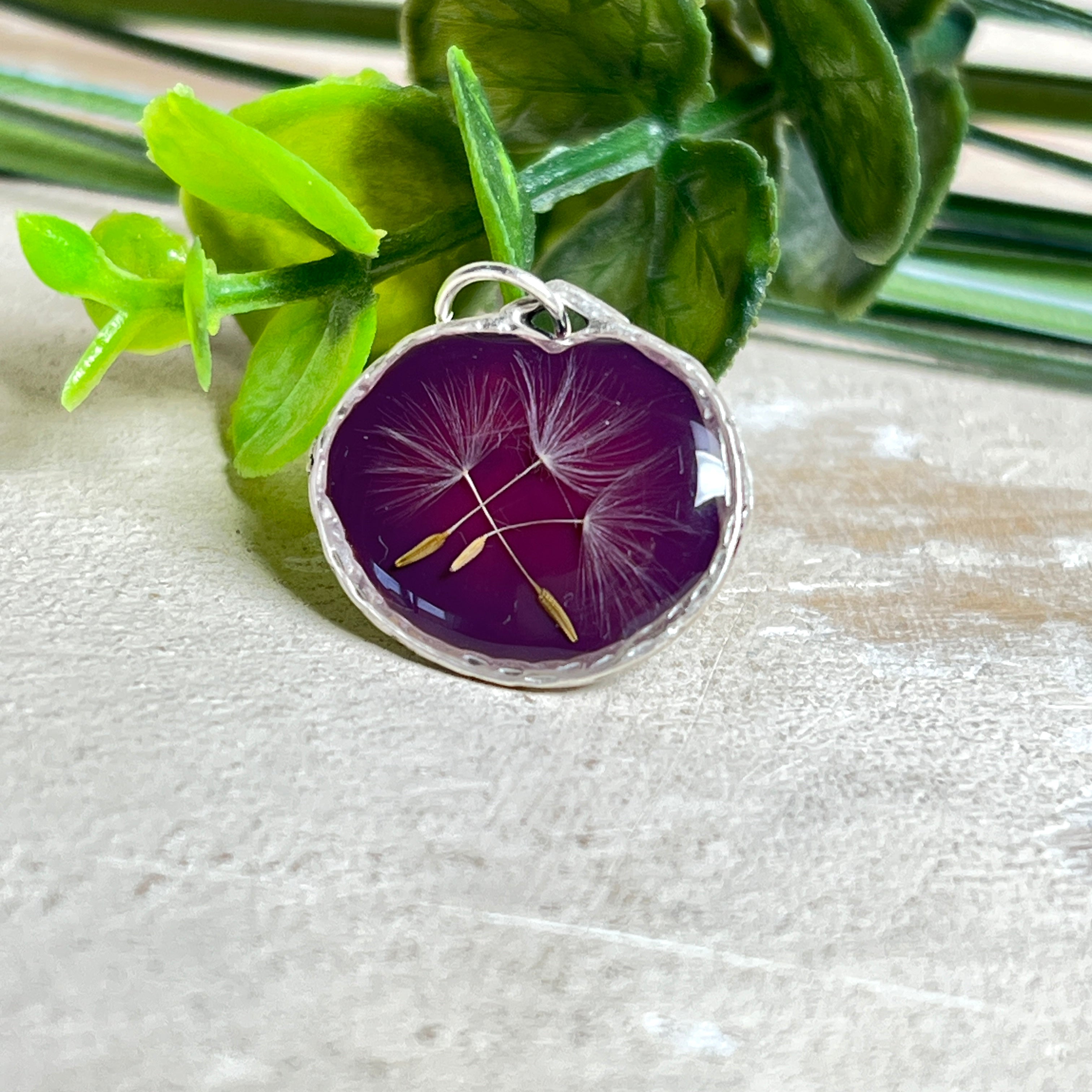 Anhänger mit echter Pusteblume in Harz, Hintergrund Brombeerfarben, Durchmesser 22 mm, nickelfreie Silberoptik-Fassung. Handgefertigtes Unikat – kleine Abweichungen möglich.