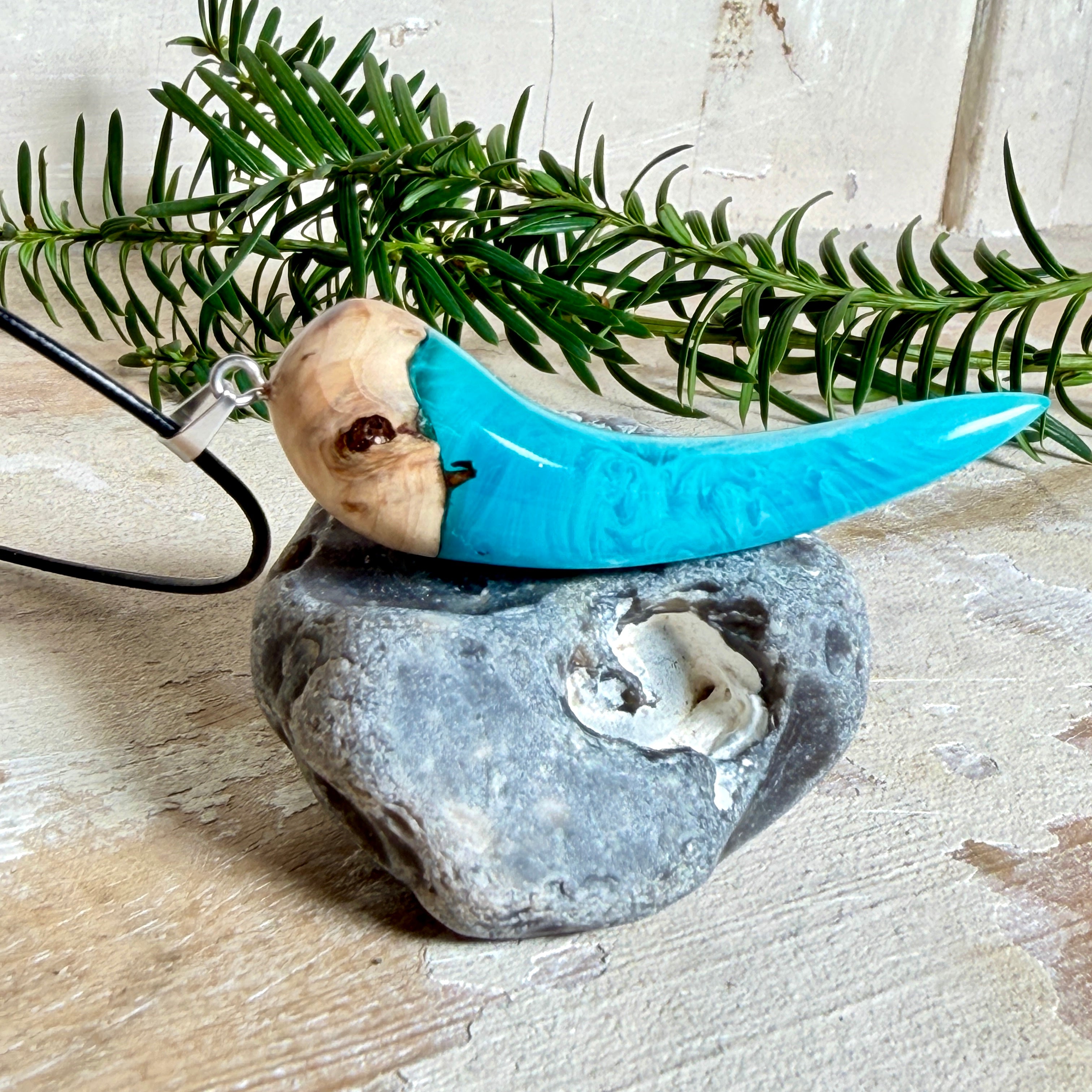 Handgefertigter Anhänger aus Edelholz und transparent-türkisblauem und weißen Epoxidharz, glatt poliert. Größe ca. 6,5 × 2,0 cm. Mit Edelstahlöse an schwarzer Lederkette (45 cm + 5 cm Edelstahl-Verlängerung, Karabiner). Moderner, unisex tragbarer Schmuck mit natürlicher Holzmaserung; kleine Lufteinschlüsse sind charakteristisch.