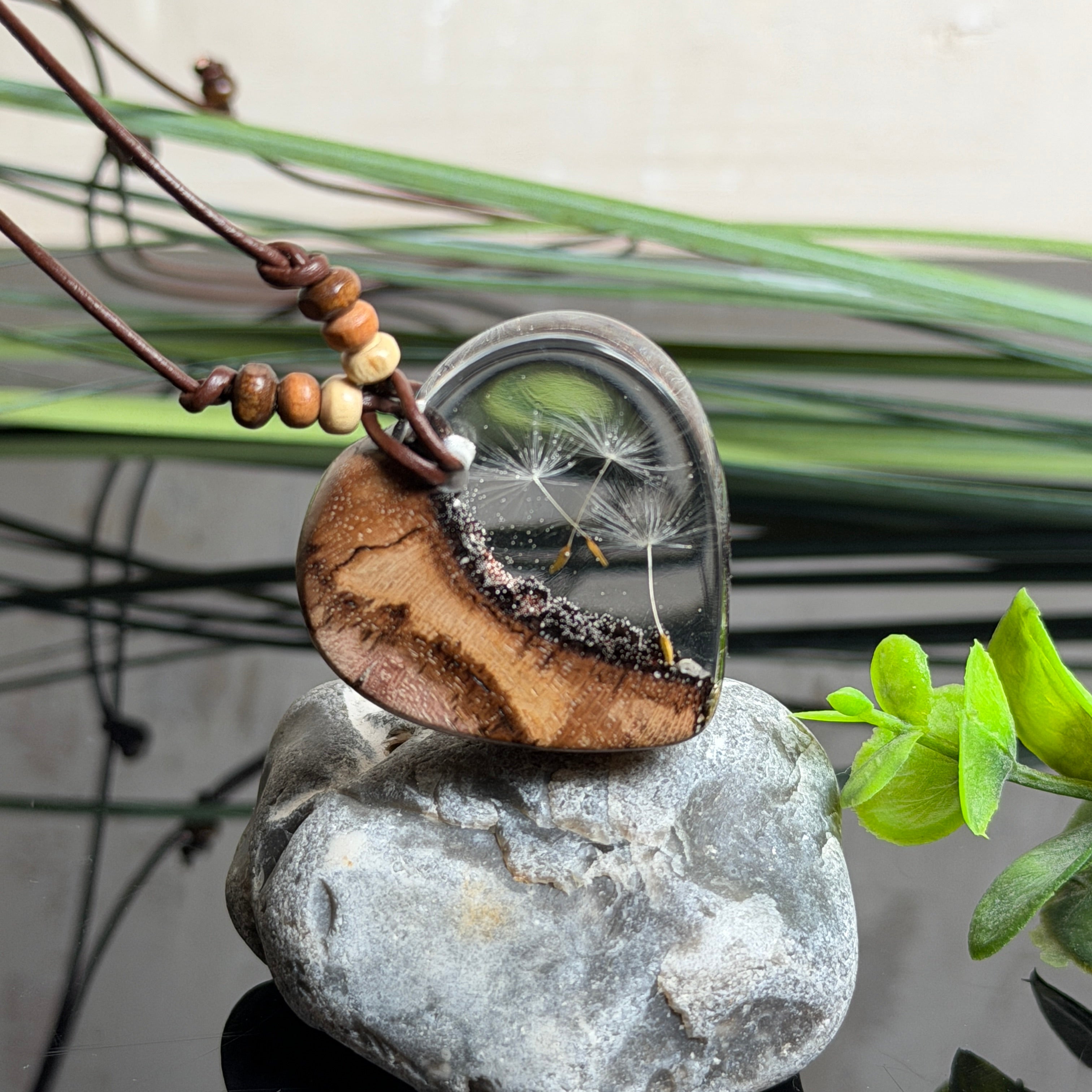 Herzanhänger „Pusteblumenzauber“ aus naturbelassenem Rebholz und klarem Epoxidharz mit schwebenden Pusteblumensamen. Dunkelbraunes, verstellbares Lederband mit kleinen Holzperlen, Anhänger ca. 3,5 × 3,5 cm. Handgefertigtes Unikat von ZeitlosSchmuckDesign.