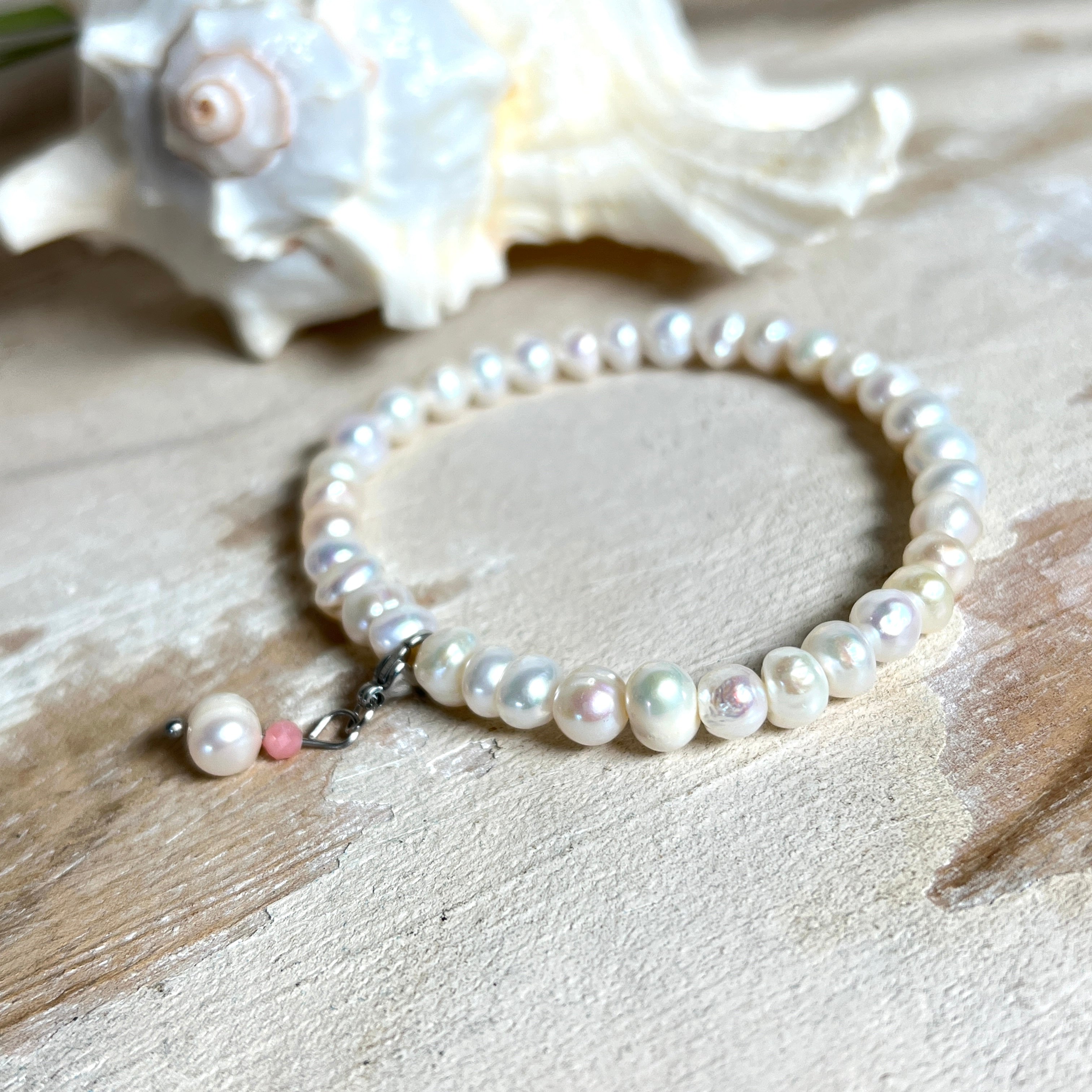 Handgefertigtes Armband „Ocean Bloom“ mit echten, schimmernden Süßwasserperlen (Ø ca. 6–7 mm) auf elastischem Band. Jede Perle ist ein Unikat mit natürlicher Form und sanftem Glanz. Highlight: Charmanhänger mit einer Süßwasserperle und einer facettierten Andenopal-Perle, befestigt an einem robusten Edelstahl-Karabiner. Ein Schmuckstück voller Eleganz, Symbolkraft und maritimer Schönheit.
