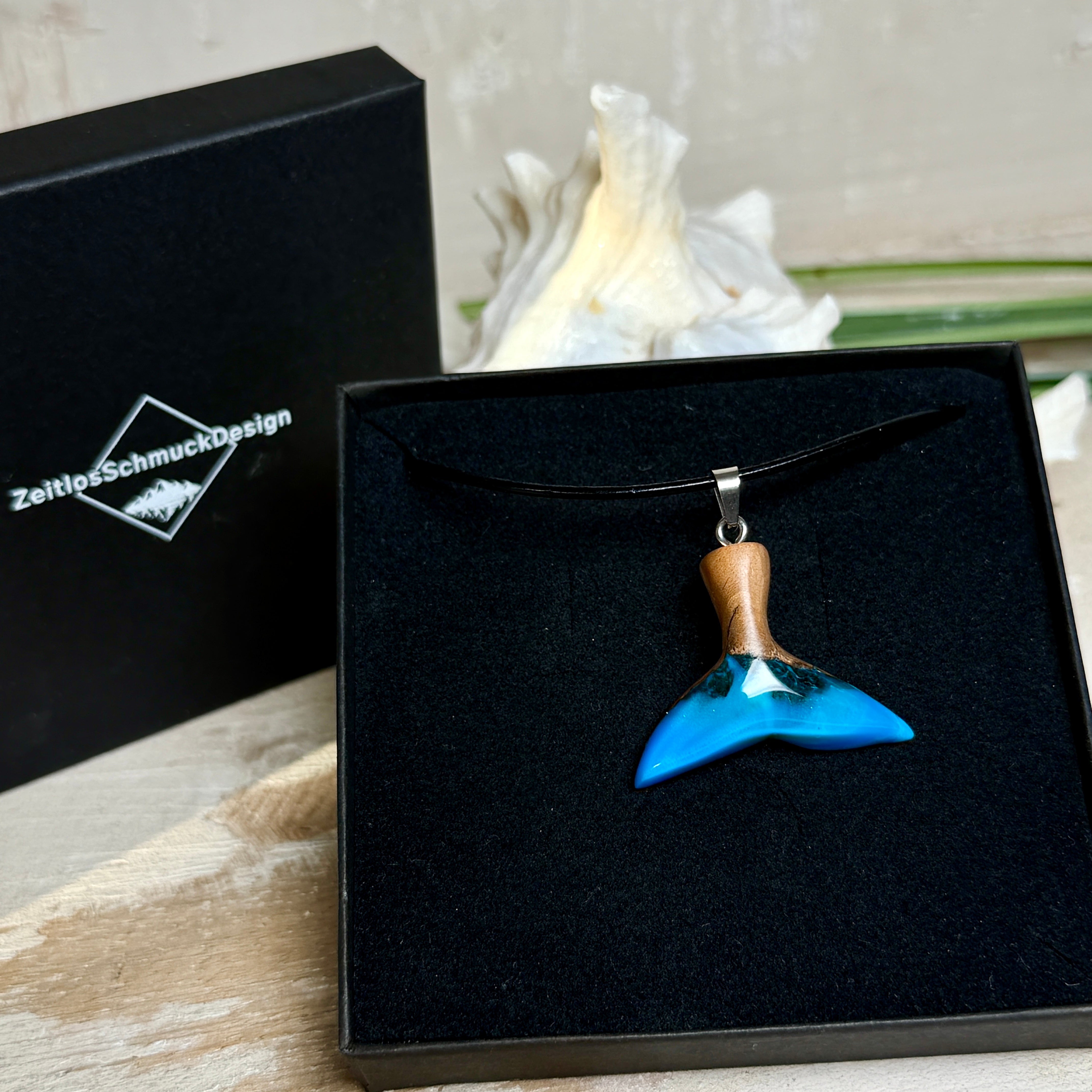 Handgefertigter Walflossen-Anhänger aus Olivenholz und Epoxidharz in Blau-Grün-Weiß, polierte Oberfläche, Edelstahl-Öse. Schwarze Lederkette 45 cm mit Edelstahl-Karabinerverschluss und 5 cm Edelstahl-Verlängerung. Anhängergröße ca. 2,5 × 3,2 cm, maritime Produktfotografie.