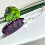 Ovaler Anhänger mit echter Pusteblume in Harz, Hintergrund Brombeerfarben. Größe 4 × 1,8 cm, versilberte Kette 50 cm mit Karabinerverschluss. Handgefertigtes Unikat.