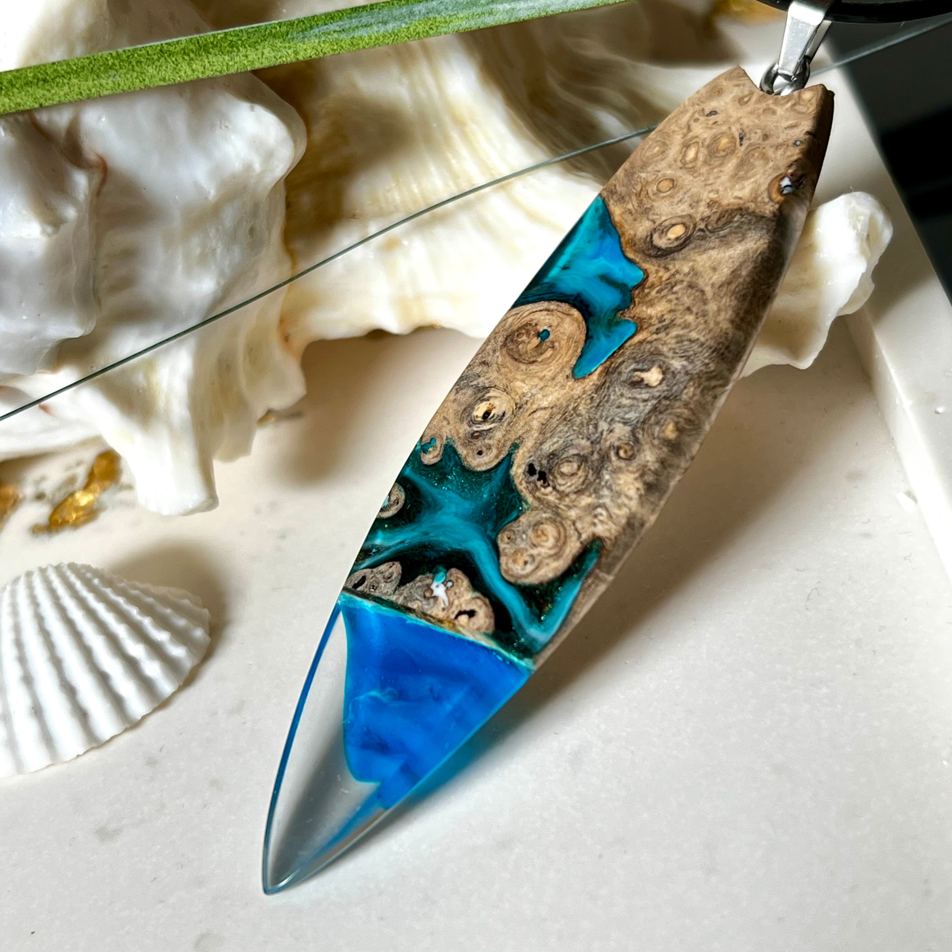 Handgefertigter Surfbrett-Anhänger aus Maserholz und transparentem Harz mit Farbverlauf in Blau und Weiß. Die natürliche Maserung des Holzes trifft auf ozeanartige Harzstrukturen. Größe ca. 6,7 x 2 cm, mit Edelstahlöse und Lederband inkl. Karabinerverschluss (45 cm + 5 cm Verlängerung). Jedes Stück ist ein Unikat – maritim, modern und mit viel Liebe gefertigt.