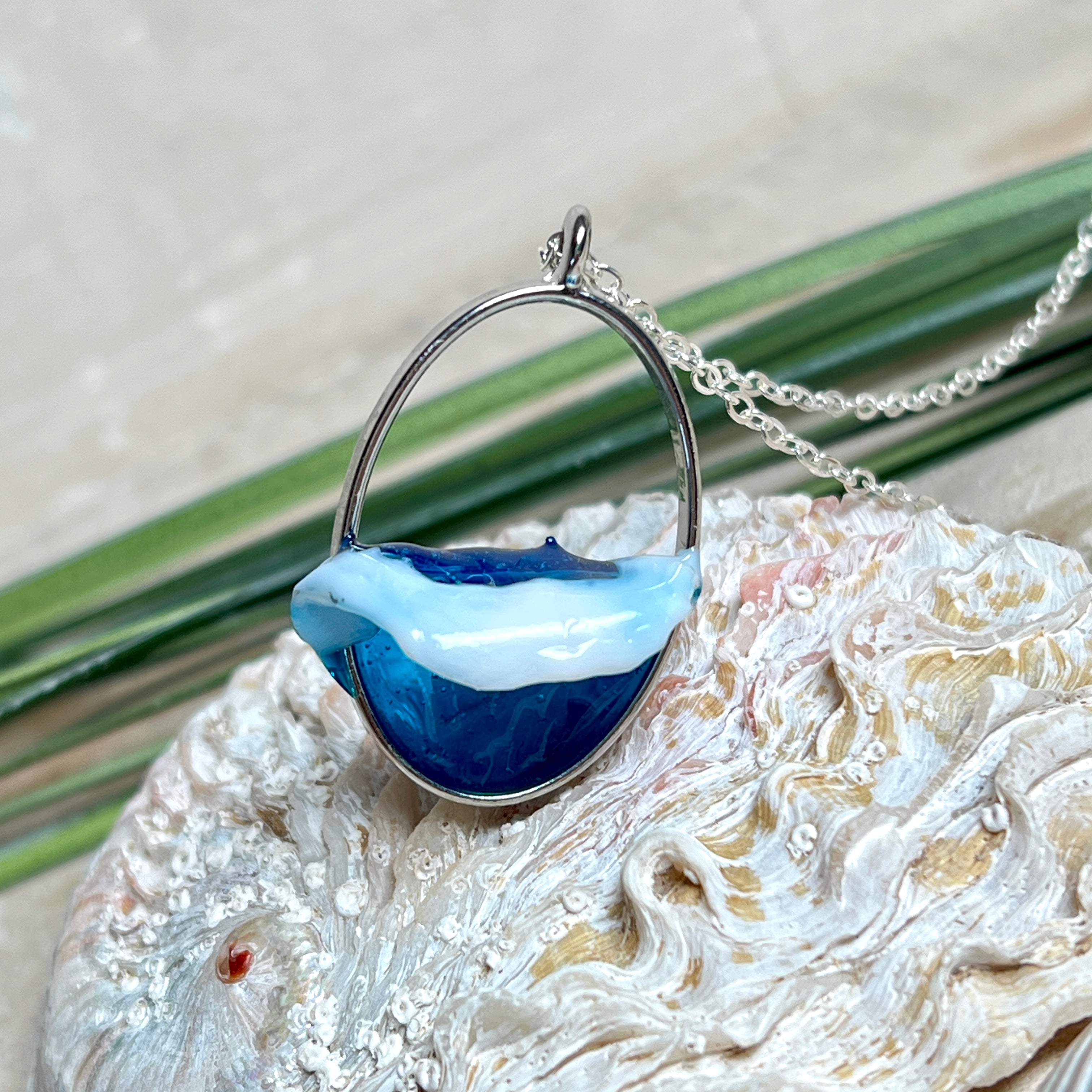 Ovale Halskette „Ocean Crest“ mit 3D-Welle: handgefertigter Harz-Anhänger in Silber-Legierung, Farbverlauf von Tiefblau zu Türkis mit weißer Schaumkrone. Größe ca. 3,9 × 2,3 cm, an einer ca. 56 cm langen versilberten Kette. Glänzende Oberfläche, maritimer Look, Unikat-Handarbeit.