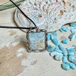 Quadratischer Larimar-Mosaik Anhänger im Edelstahlrahmen mit Seestern-Element und facettierter Bergkristall-Perle, eingebettet in Harz, an schwarzer Lederkette.