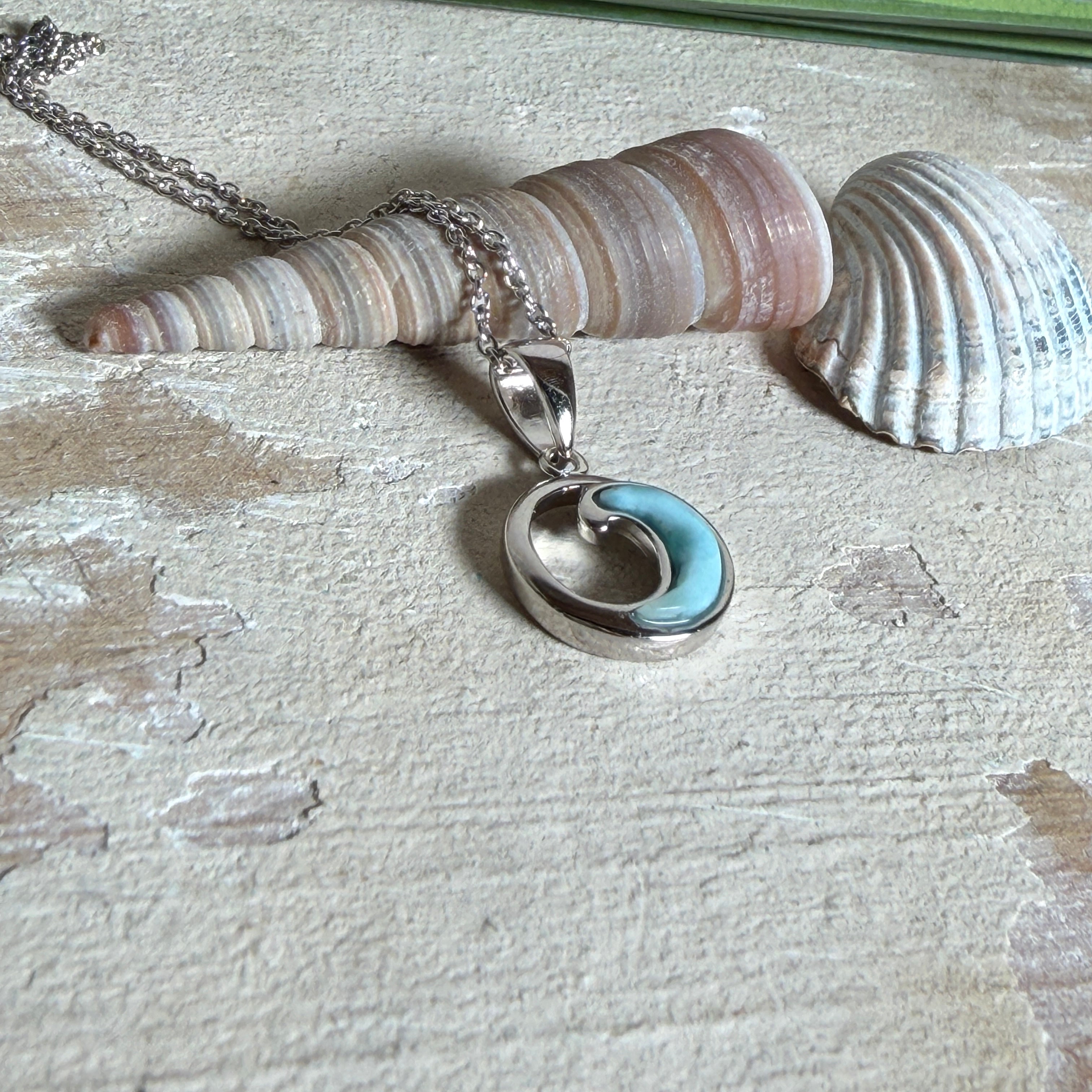 Feine Wellen-Kette aus rhodiniertem 925 Silber. Der runde Anhänger zeigt eine stilisierte Welle mit hellblauem Larimar-Cabochon, eingefasst in poliertem Silber. Größe des Anhängers ca. 23 x 13 mm, an einer 45 cm langen, 1 mm starken, rhodinierten Silberkette. 