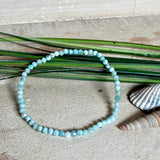 Zartes Larimar-Armband „Lagunenlicht“ mit facettierten 3 mm Perlen aus seltenem Atlantisstein auf Elastikfaden. Die kleinen Larimarsteine zeigen sanfte Blau- und Weißtöne wie Lagunenwasser. Innenumfang ca. 19 cm. Fotografiert auf Muscheln, einem dekorativen Stein und in einer schwarzen Schmuckbox von ZeitlosSchmuckDesign im maritimen Stil.
