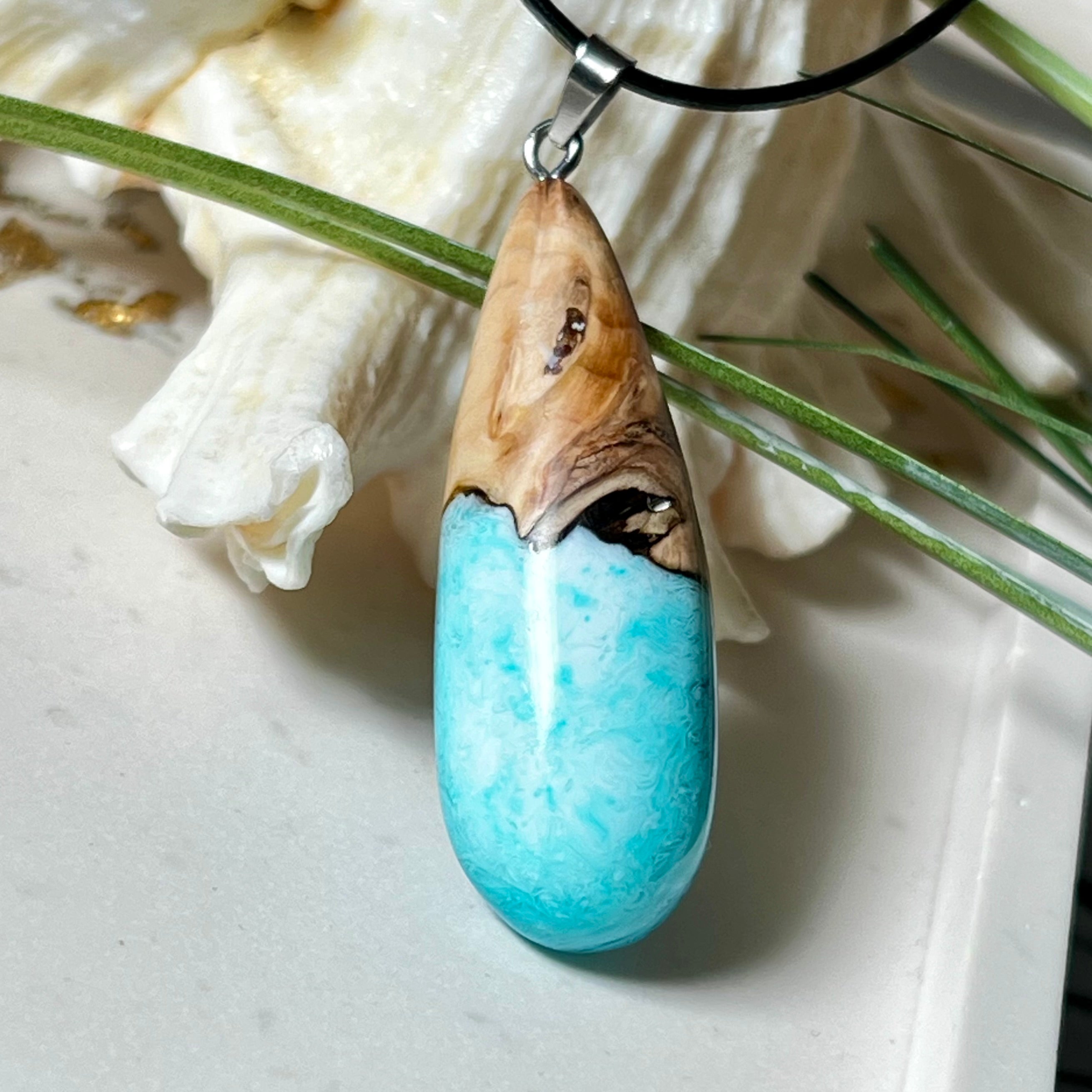 Tropfenförmiger Anhänger aus Maserholz und Harz in leuchtenden Blautönen und Weiß. Inspiriert vom Meer, in Handarbeit gegossen,gesägt, geschliffen und hochglanzpoliert. Mit verstellbarer Lederkette (45 + 5 cm) und Edelstahlkarabiner. Jeder Anhänger ist ein Unikat mit natürlicher Maserung. Ein maritimes Schmuckstück für Naturfreunde und alle, die das Wasser lieben.