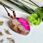 Handgefertigter Herzanhänger aus Olivenholz und leuchtend pinkem Epoxidharz mit eingeschlossenen Pusteblumensamen. Verstellbares braunes Lederband mit Holzperlen, Anhänger ca. 3,5 × 3,3 cm groß. Das Harz leuchtet dezent unter Schwarzlicht. Ein einzigartiges Unikat von ZeitlosSchmuckDesign, inspiriert von Kindheitsglück und Pusteblumen.