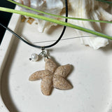 Handgefertigter Anhänger in Seesternform aus echtem Meersand und transparentem Harz. Verziert mit einer natürlichen Süßwasserperle. Edelstahlöse, Lederkette mit Karabinerverschluss (45 cm + 5 cm Verlängerung). Maritimer Schmuck im Unikatcharakter – inspiriert vom Meer und handgefertigt mit Liebe zum Detail. Perfektes Geschenk für Strandliebhaber.