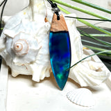Beidseitig tragbarer Surfbrett-Anhänger aus Olivenholz, kombiniert mit klaren Epoxidharz in Blau-Grün. Eingearbeiteter synthetischer Opal erzeugt ein faszinierendes Farbspiel wie Nordlichter. Größe ca. 6 × 1,8 cm. Mit verstellbarem Lederband (26–45 cm), dekorativen Perlen & Schiebeknoten. Handgefertigt & einzigartig. Ein Schmuckstück mit Naturinspiration.