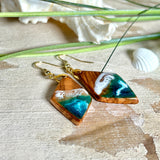 Handgefertigte Ohrringe „Ocean Diamond“ aus Olivenholz und Epoxidharz in Diamantform. Türkis-, Blau- und Weißtöne bilden ein wellenartiges Design, inspiriert vom Meer. Jeder Ohrring ist ein Unikat mit individueller Maserung. Vergoldete, nickelfreie und bleifreie Anhängerschlaufe, 925 Sterling Silber Ohrhaken. Maritimer Schmuck für Meerliebhaber und besondere Anlässe.