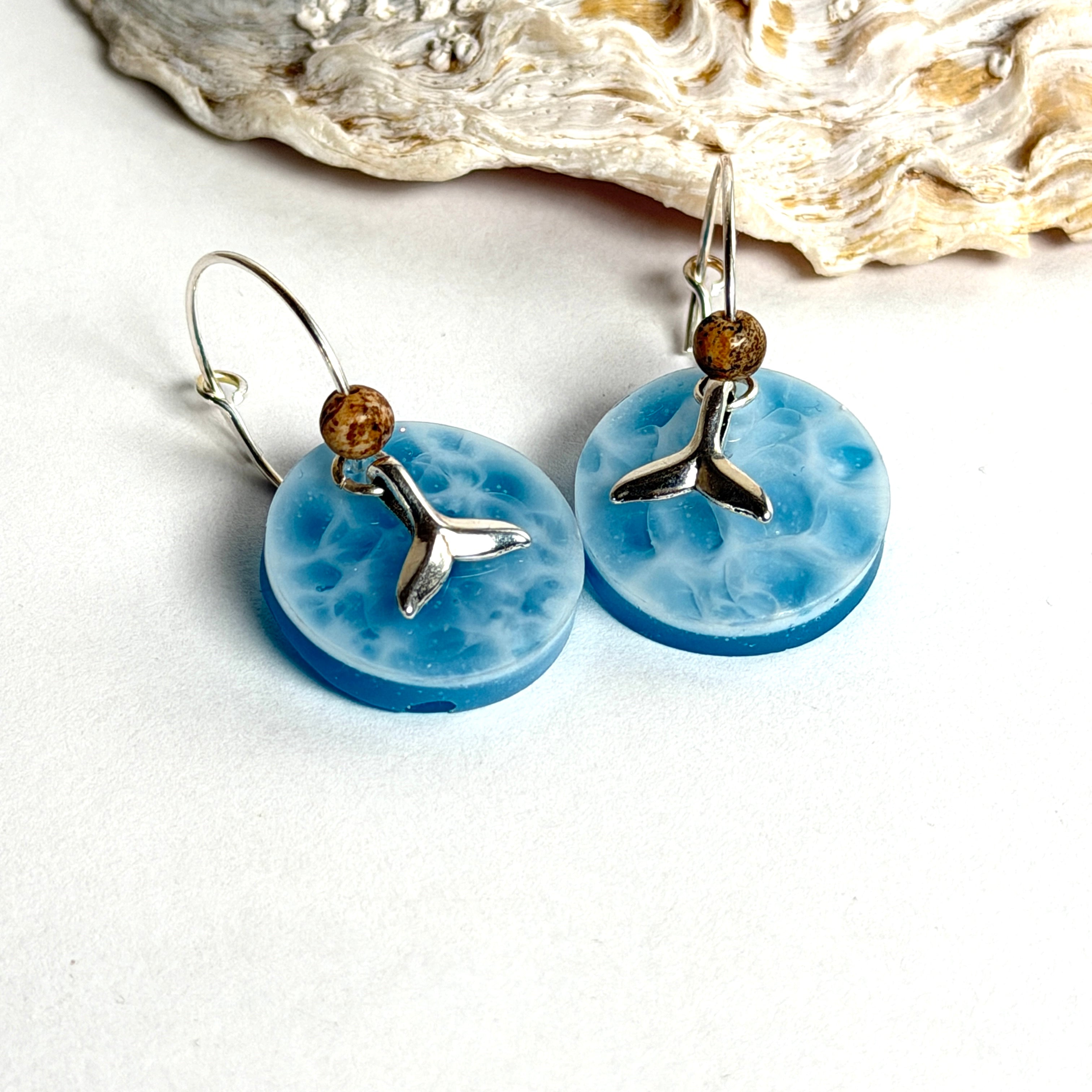 Handgefertigte Creolen-Ohrringe mit hellblauer Resin-Scheibe, zarter Wolkenmarmorierung, silbernem Walflosse-Charm und Jaspis-Natursteinperle. 925 Silber Creole, Gesamtlänge ca. 3,5 cm – Ocean-Feeling für jeden Tag.