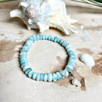 Handgefertigtes Armband aus seltenem Larimar mit facettierten, türkis-blauen Edelsteinperlen (Ø ca. 6–7 mm), elastischem Band und einem zarten Süßwasserperlen-Charm an Edelstahlkarabiner. Der wertvolle Larimar, auch „Stein des Atlantis“ genannt, gilt als Edelstein der Ruhe und Meeresverbundenheit.