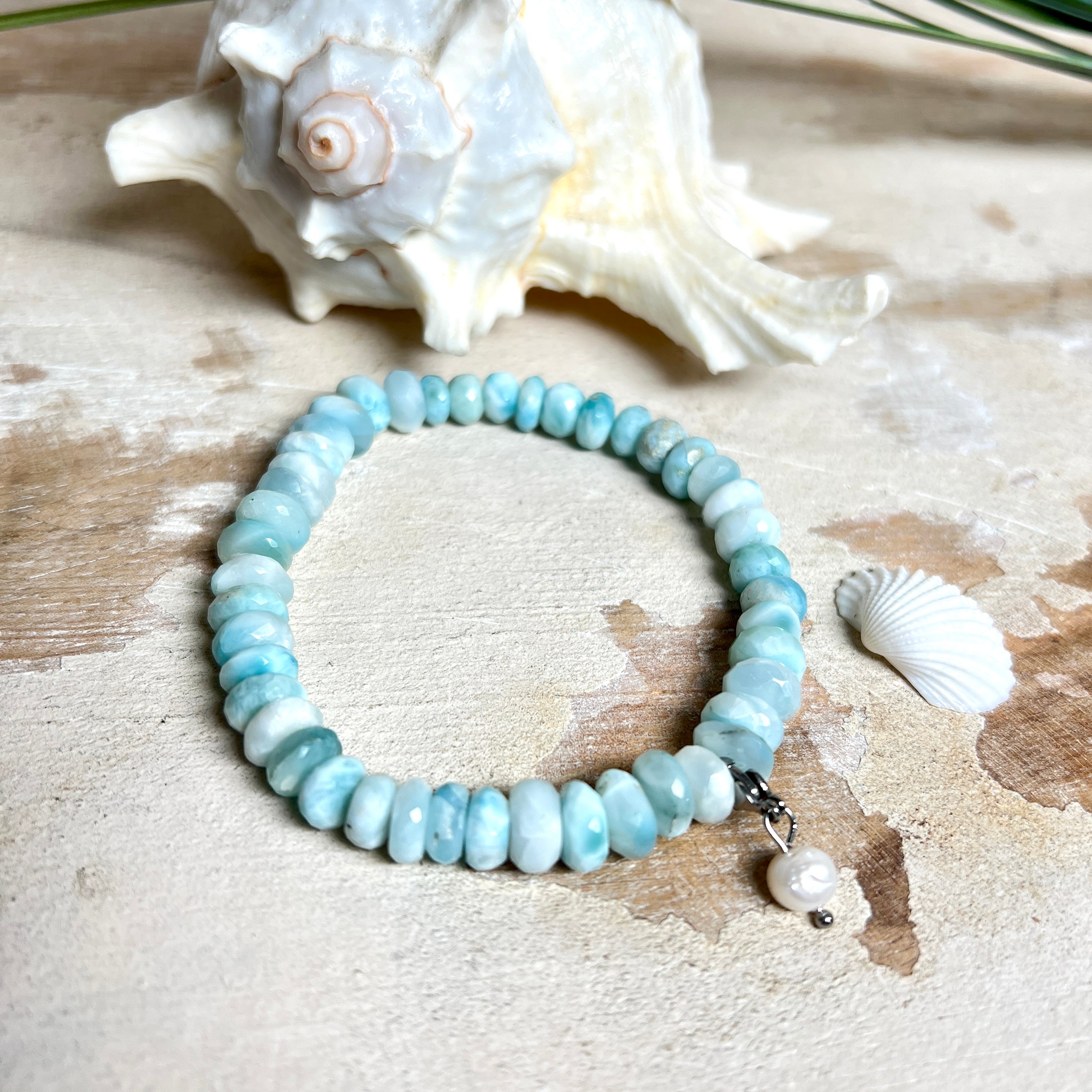 Handgefertigtes Armband aus seltenem Larimar mit facettierten, türkis-blauen Edelsteinperlen (Ø ca. 6–7 mm), elastischem Band und einem zarten Süßwasserperlen-Charm an Edelstahlkarabiner. Der wertvolle Larimar, auch „Stein des Atlantis“ genannt, gilt als Edelstein der Ruhe und Meeresverbundenheit.