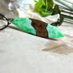 Anhänger aus Nussbaumholz und fluoreszierendem Epoxidharz in Grün-Weiß. Größe ca. 5,8 × 2 cm, Edelstahlöse, Lederkette 45+5 cm. Handgefertigtes Unikat.