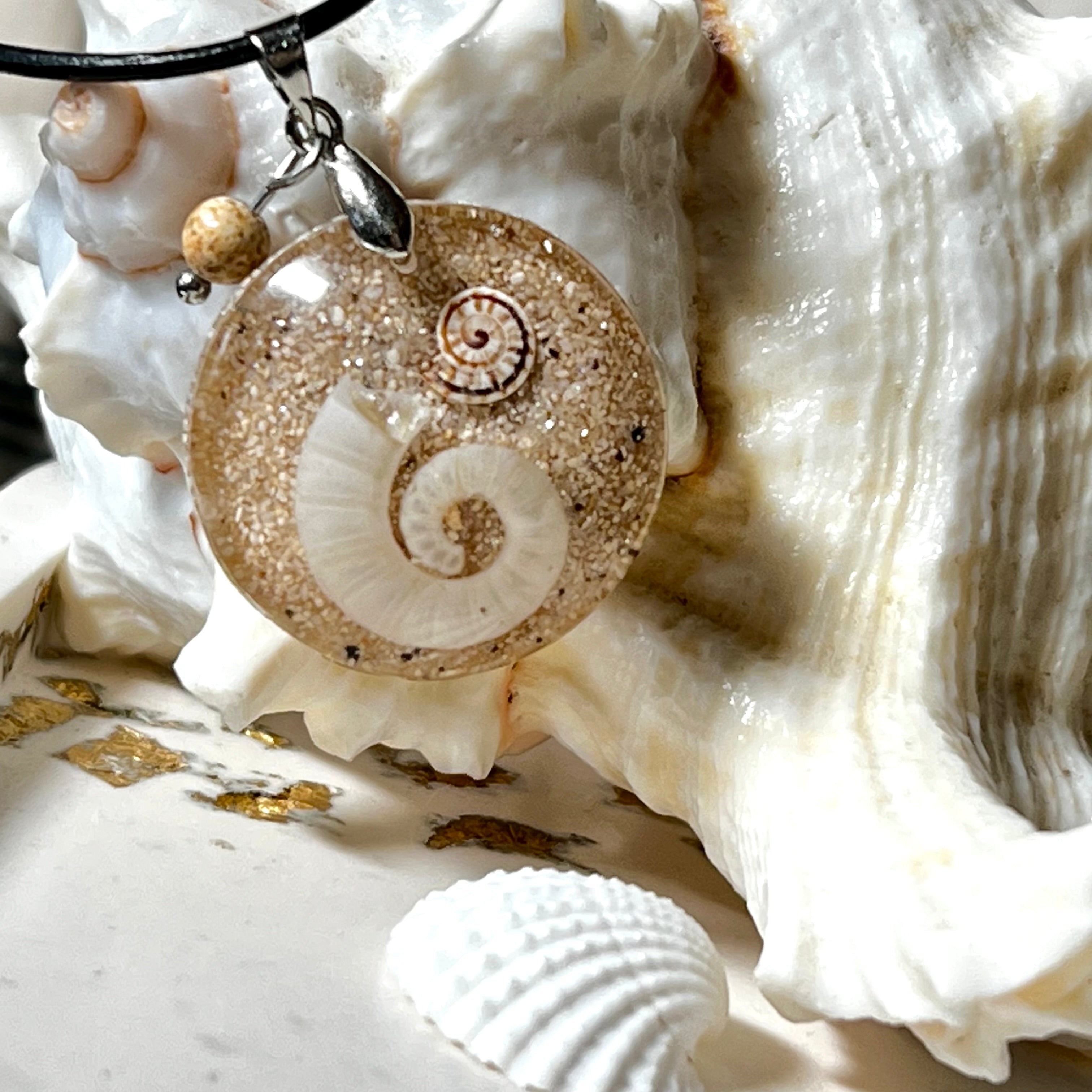 Handgemachter Anhänger mit echter Spirale, kleiner Schnecke, Meersand und feinem Glitzereffekt im Harz. Verziert mit einer Jaspisperle, Edelstahlöse und Lederkette mit Verlängerung. Maritimer Natur-Schmuck, inspiriert vom Ozean