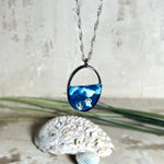 „Riffschatz“ – ovaler Harz-Anhänger mit plastischer 3D-Welle in Blau/Türkis, weißer Schaumkrone und Muschel-/Korallen-Stickern am Grund. Die Sticker sind unter klarem Harz versiegelt. Silber-Legierung, ca. 3,9 × 2,3 cm, an einer ca. 56 cm langen versilberten Kette. Handgefertigt, hochglänzend, jedes Stück ein Unikat.