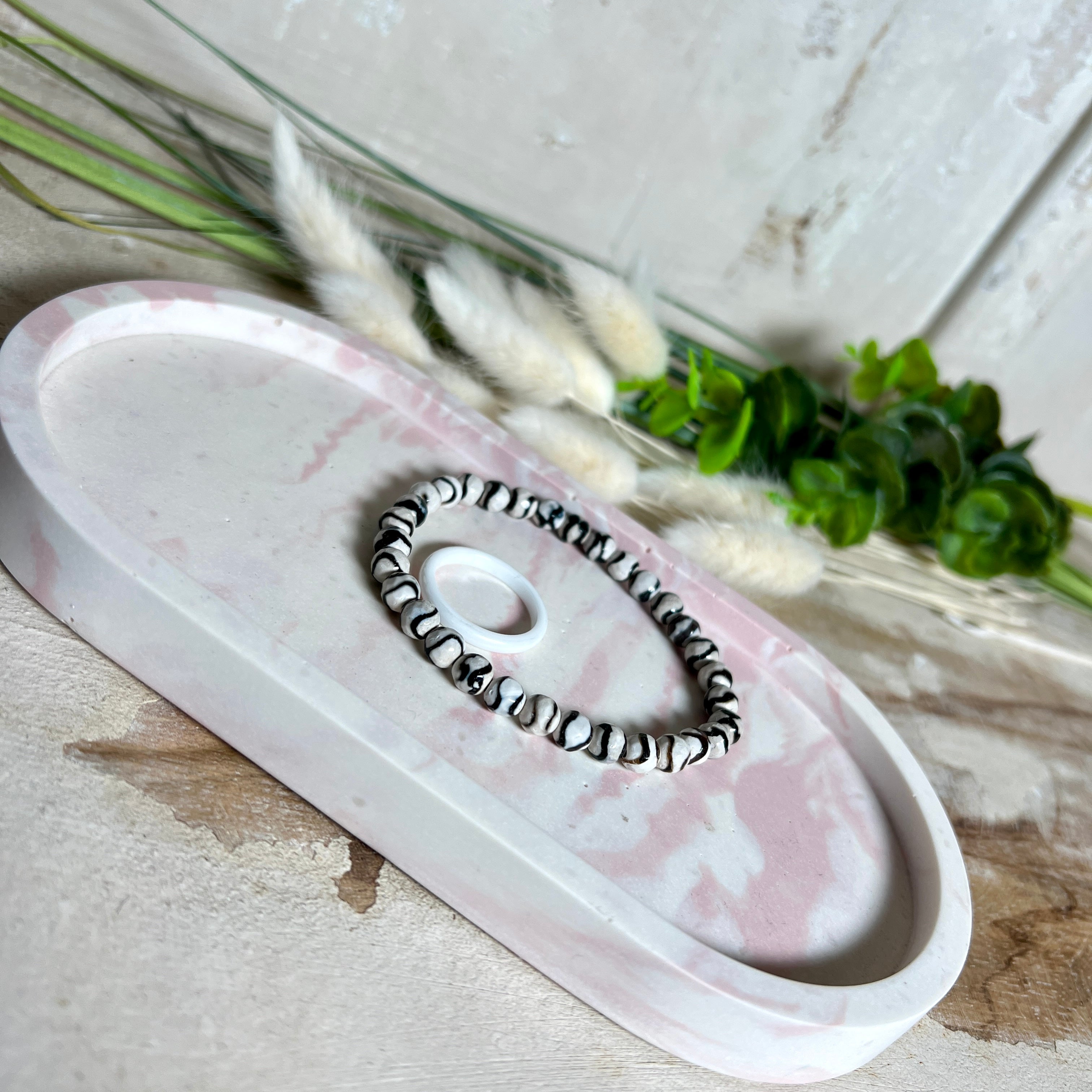 Schmucktablett aus Jesmonite in zartem Rosa-Weiß-Marmor. Handgegossenes, ovales Deko-Tablett mit glatter Oberfläche und Korkfüßen. Perfekt als Ablage für Schmuck, Schlüssel, Brille oder Dekoobjekte. Jedes Stück ein liebevoll gefertigtes Unikat in der Größe 17,5 × 9,5 × 1,7 cm.