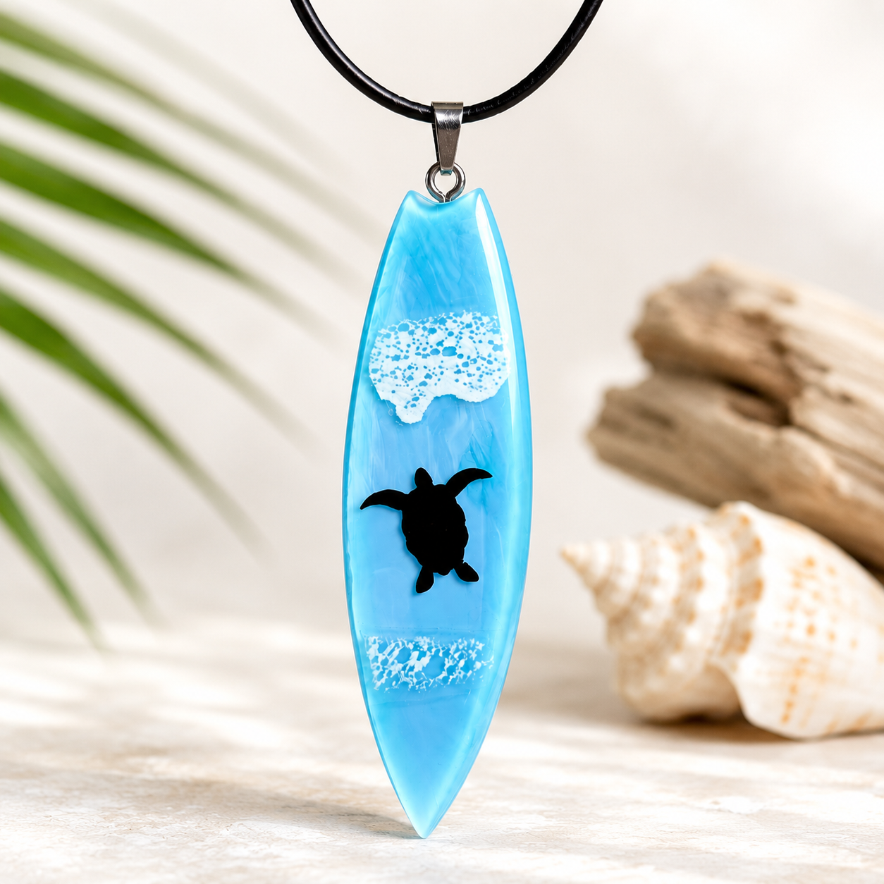 Handgefertigter Surfbrett Anhänger aus hellblauem Epoxidharz mit schwarzer Meeresschildkröte und weißen Wellenmotiven. Maritimer Unisex Schmuck an schwarzer Lederkette. Hochglanz poliertes Unikat inspiriert von Meer, Strand und Ozean.