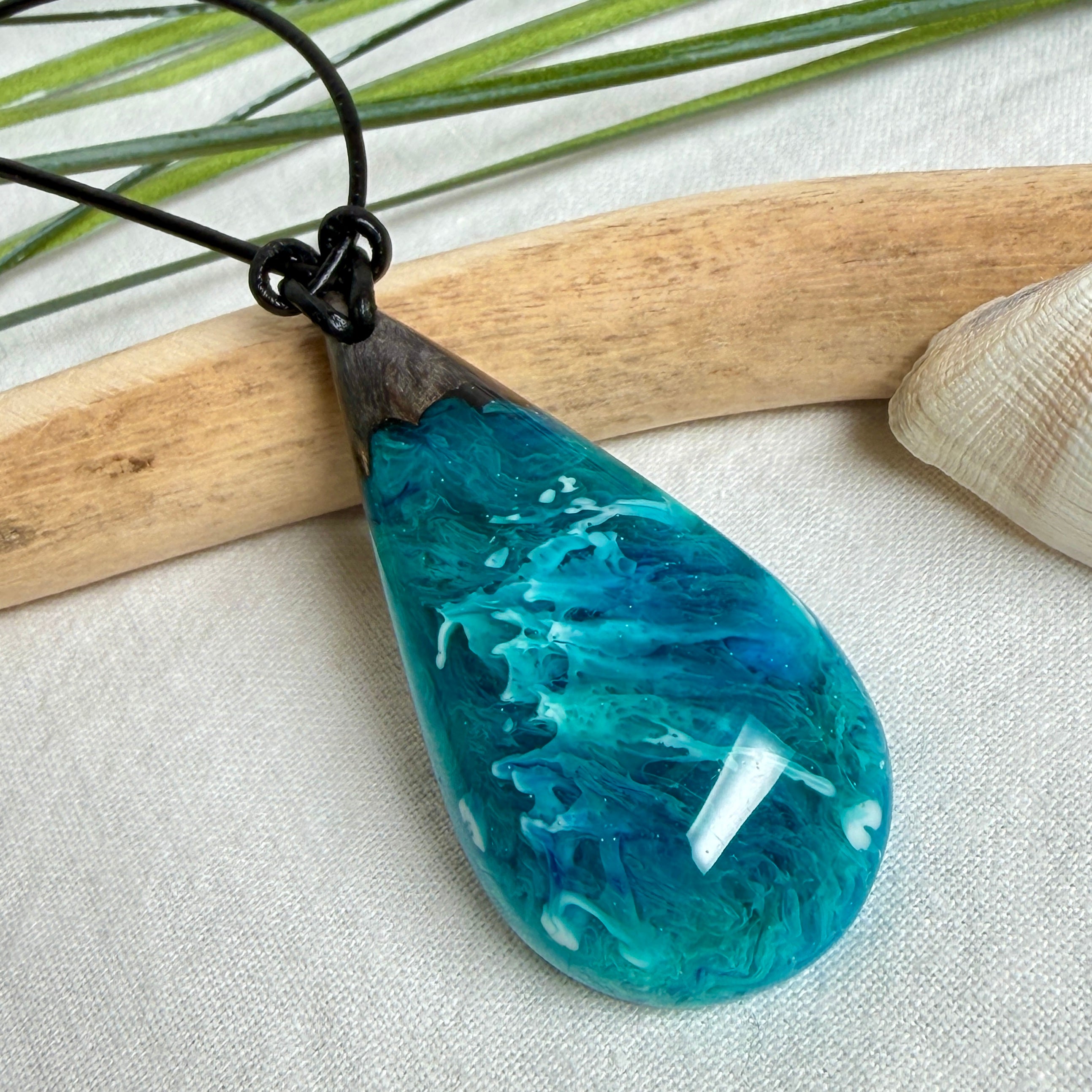 Tropfen Anhänger aus dunklem Maserholz und Epoxidharz in Türkis Blau mit weißer Wellenstruktur am schwarzen Lederband, maritimer Holz Harz Naturschmuck
