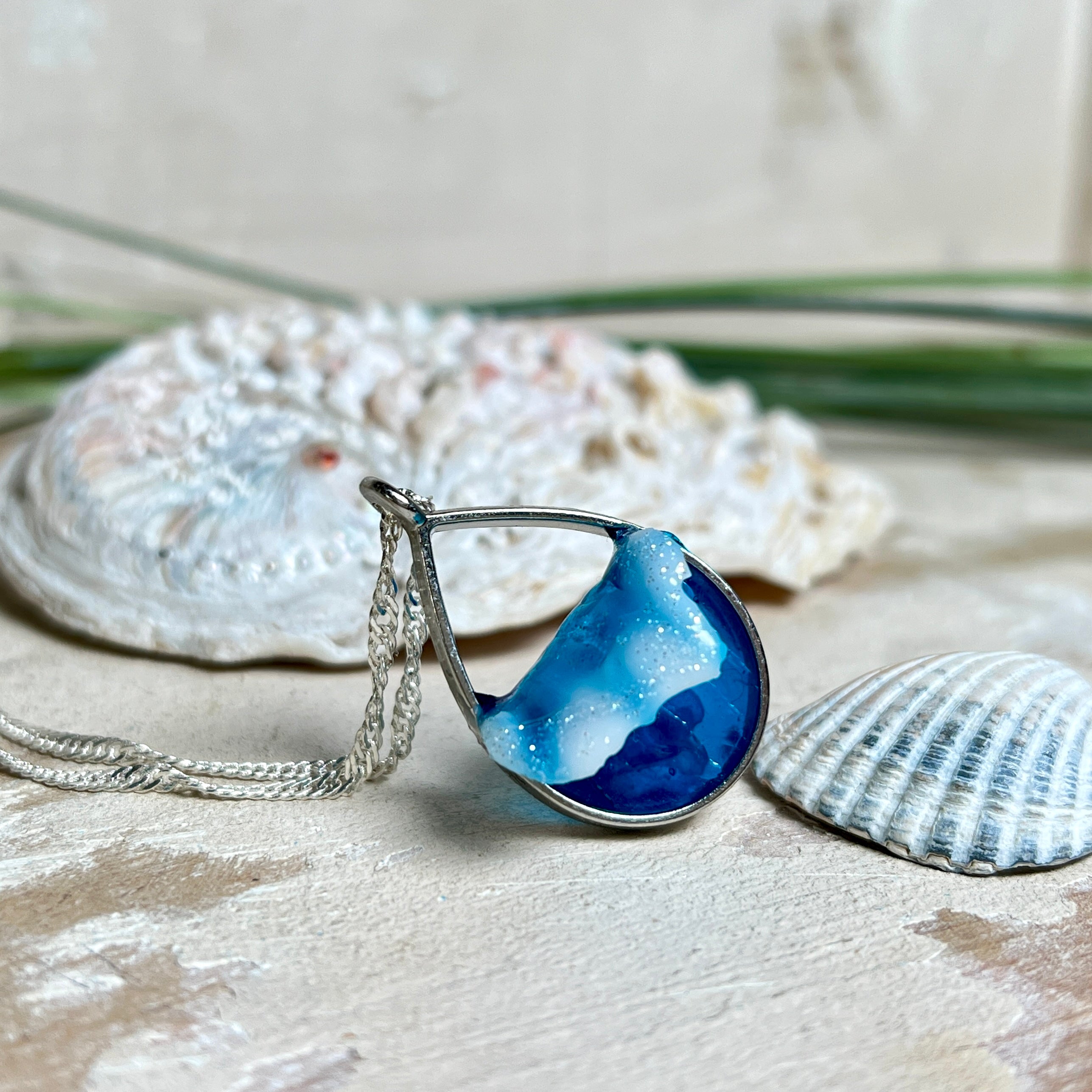 „Lagunenlicht“ – Tropfenanhänger mit handmodellierter 3D-Welle und feinem Glitzereffekt. Klarer Harzlook in Blau/Türkis, gefasst in Silber-Legierung. Größe ca. 3,5 × 2 cm. Geliefert an einer versilberten Kette (ca. 56 cm). Hochglänzend , maritimer Unikatcharakter.