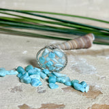 Runder Anhänger „Atlantis Dream“ aus antik-silberfarbener Zinklegierung, gefüllt mit kleinen Larimar-Edelsteinchen und klarem Resin. Die Larimarsteine zeigen sanfte Blau- und Weißtöne, die an das Meer erinnern. Durchmesser ca. 22 mm, handgefertigtes Unikat, fotografiert auf maritimem Untergrund mit kleinen Larimarsteinen und Muscheln zur Größenorientierung.