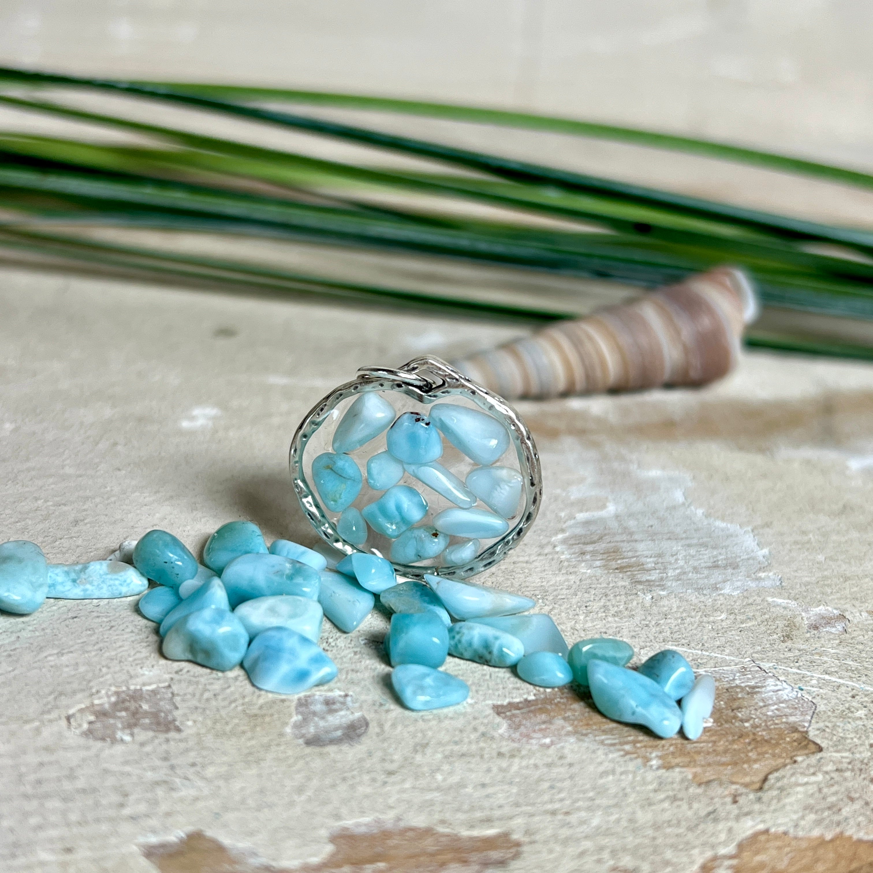 Runder Anhänger „Atlantis Dream“ aus antik-silberfarbener Zinklegierung, gefüllt mit kleinen Larimar-Edelsteinchen und klarem Resin. Die Larimarsteine zeigen sanfte Blau- und Weißtöne, die an das Meer erinnern. Durchmesser ca. 22 mm, handgefertigtes Unikat, fotografiert auf maritimem Untergrund mit kleinen Larimarsteinen und Muscheln zur Größenorientierung.