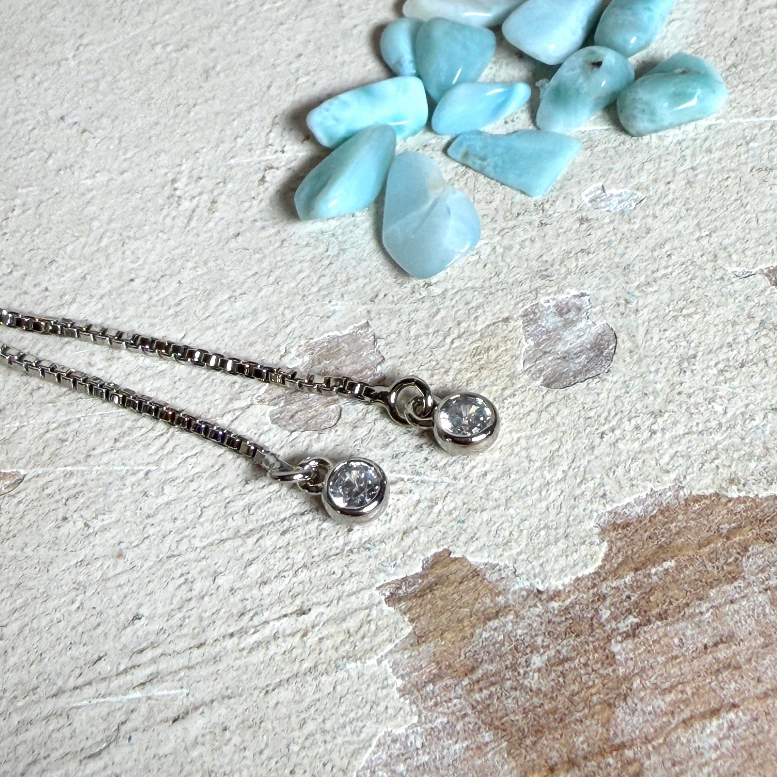 Verstellbares Edelstahlarmband mit Zirkoniasteinchen und Schiebeverschluss und rundem Anhänger (ca. 2,5 × 1,7 cm) mit echten Larimar-Edelstein-Splittern in Harz. Zusätzlich ein Charm „Blume des Lebens“ aus 925 Silber. Handgefertigtes Unikat in Türkis- und Meeresblautönen – Schmuckstück in Nahaufnahme bzw. als Tragebild am Handgelenk.