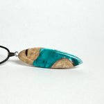 Handgefertigte Surfbrett Kette aus Maserholz und türkisfarbenem Resin mit Edelstahl Anhängerschlaufe an schwarzer Lederkette mit Karabiner und Verlängerung. Filigraner Ocean Anhänger inspiriert von Meer und Wellen, natürlicher Unikat Schmuck für Damen und Herren.