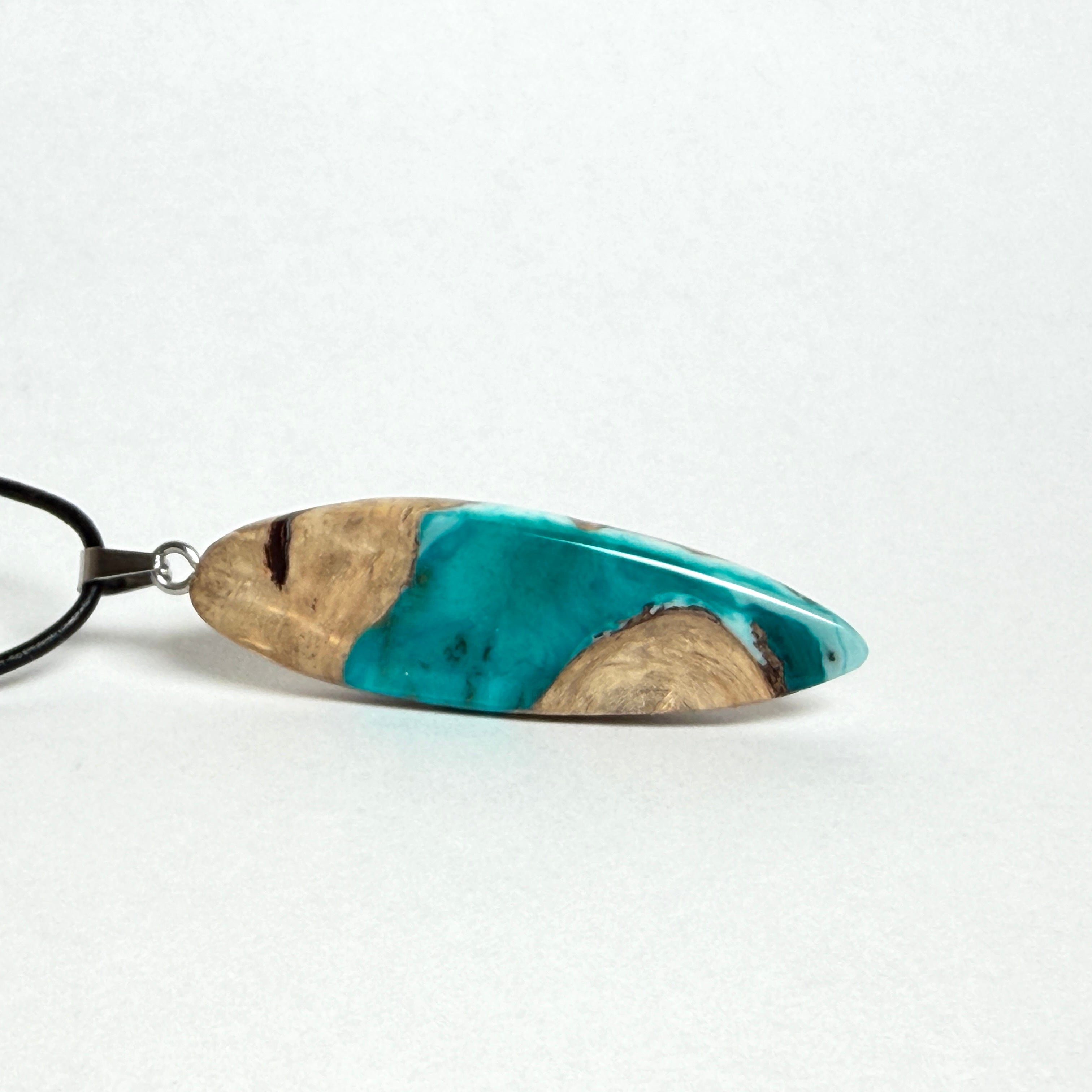 Handgefertigte Surfbrett Kette aus Maserholz und türkisfarbenem Resin mit Edelstahl Anhängerschlaufe an schwarzer Lederkette mit Karabiner und Verlängerung. Filigraner Ocean Anhänger inspiriert von Meer und Wellen, natürlicher Unikat Schmuck für Damen und Herren.
