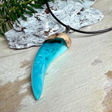 Handgefertigter Anhänger aus Edelholz und transparent-türkisblauem und weißen Epoxidharz, glatt poliert. Größe ca. 6,5 × 2,0 cm. Mit Edelstahlöse an schwarzer Lederkette (45 cm + 5 cm Edelstahl-Verlängerung, Karabiner). Moderner, unisex tragbarer Schmuck mit natürlicher Holzmaserung; kleine Lufteinschlüsse sind charakteristisch.