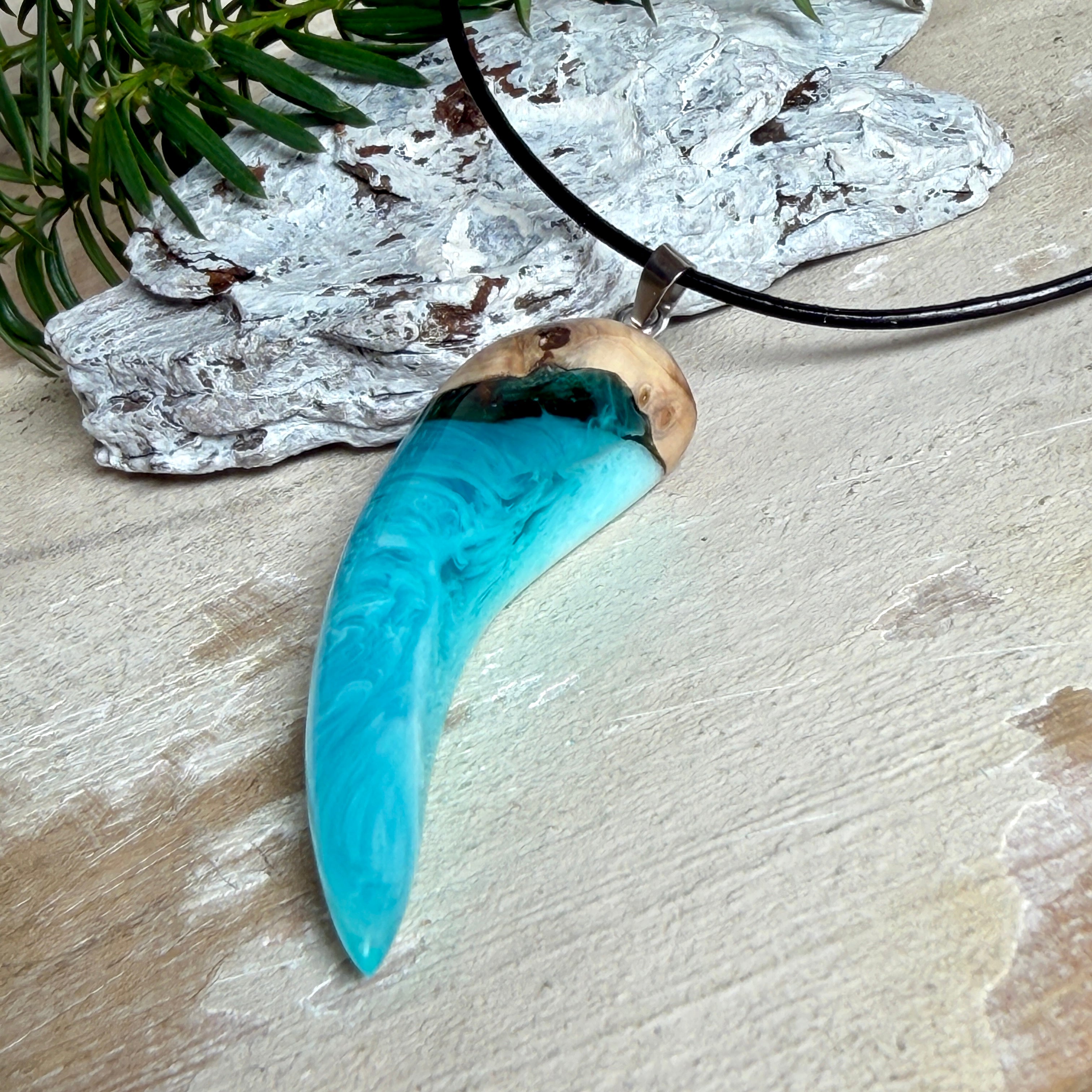 Handgefertigter Anhänger aus Edelholz und transparent-türkisblauem und weißen Epoxidharz, glatt poliert. Größe ca. 6,5 × 2,0 cm. Mit Edelstahlöse an schwarzer Lederkette (45 cm + 5 cm Edelstahl-Verlängerung, Karabiner). Moderner, unisex tragbarer Schmuck mit natürlicher Holzmaserung; kleine Lufteinschlüsse sind charakteristisch.