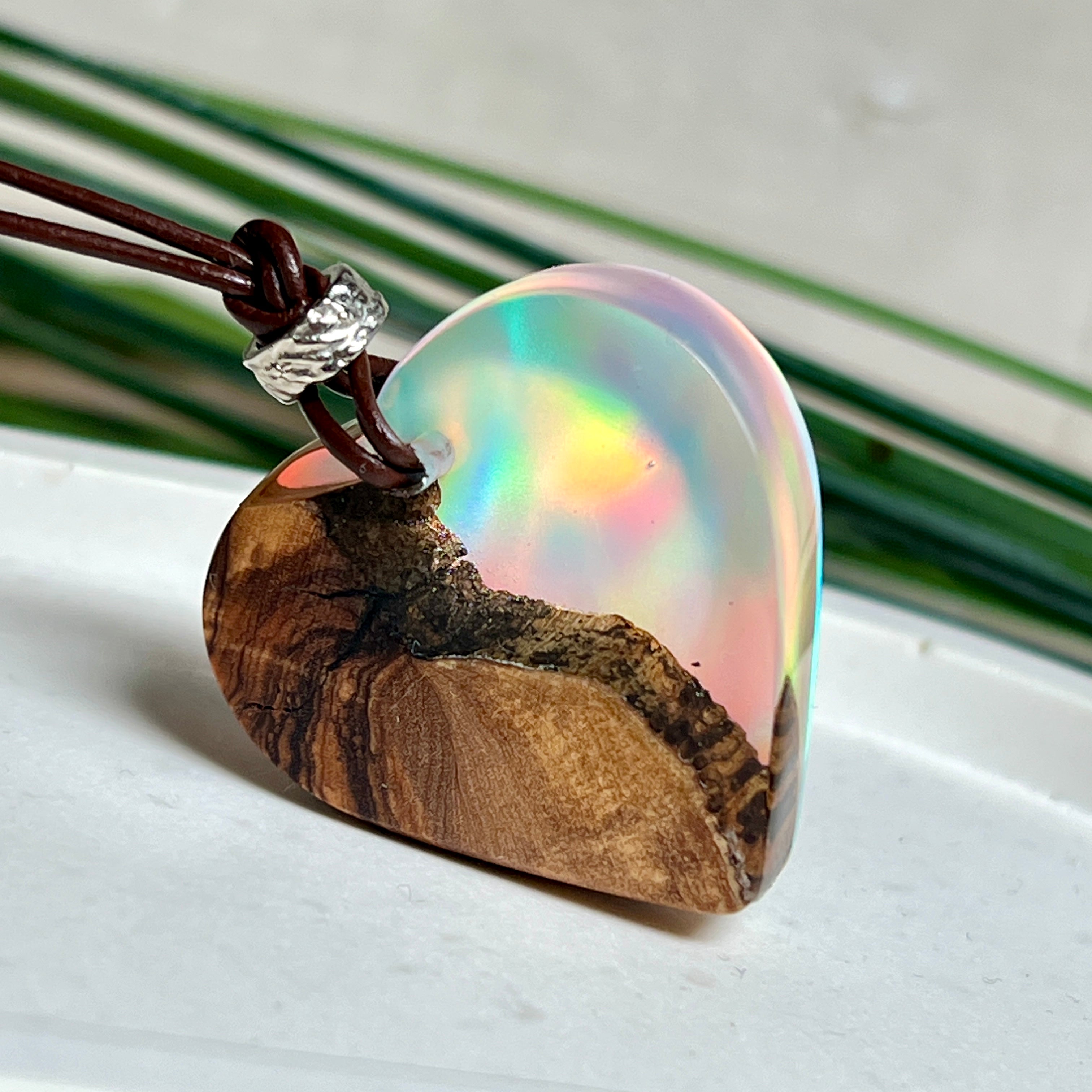 Handgefertigter Herzanhänger aus Olivenholz und schimmerndem Opalharz (Resin Colloidal Imitation Opal) – ein hochwertiges Harz mit feinen, lichtreflektierenden Partikeln, die an echte Opale erinnern. Je nach Licht schimmert der Anhänger in Regenbogenfarben. Mit braunem Lederband und silberfarbener Perle. Jedes Stück ein liebevoll gefertigtes Unikat.