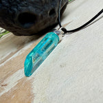 Nahaufnahme einer handgefertigten Halskette mit Aqua Aura Rohkristall: naturbelassener, sechskantiger Bergkristall mit goldbedampfter Aqua-Beschichtung in Türkisblau, gefasst in 925er Silber und getragen an einer schwarzen Lederkette mit Edelstahl-Karabiner und Verlängerungskettchen.