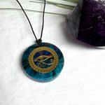 Runder Anhänger mit goldenem Horusauge aus Metall in blau türkis violettem Epoxidharz am schwarzen Baumwollband, spiritueller Eye of Ra Naturschmuck Amulett