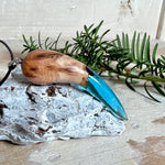 Handgefertigter Anhänger aus Edelholz und transparent-türkisblauem Epoxidharz, glatt poliert. Größe ca. 6,7 × 2,0 cm. Mit Edelstahlöse an schwarzer Lederkette (45 cm + 5 cm Edelstahl-Verlängerung, Karabiner). Maritimer, moderner Unisex-Schmuck mit natürlicher Holzmaserung; kleine Lufteinschlüsse sind charakteristisch.