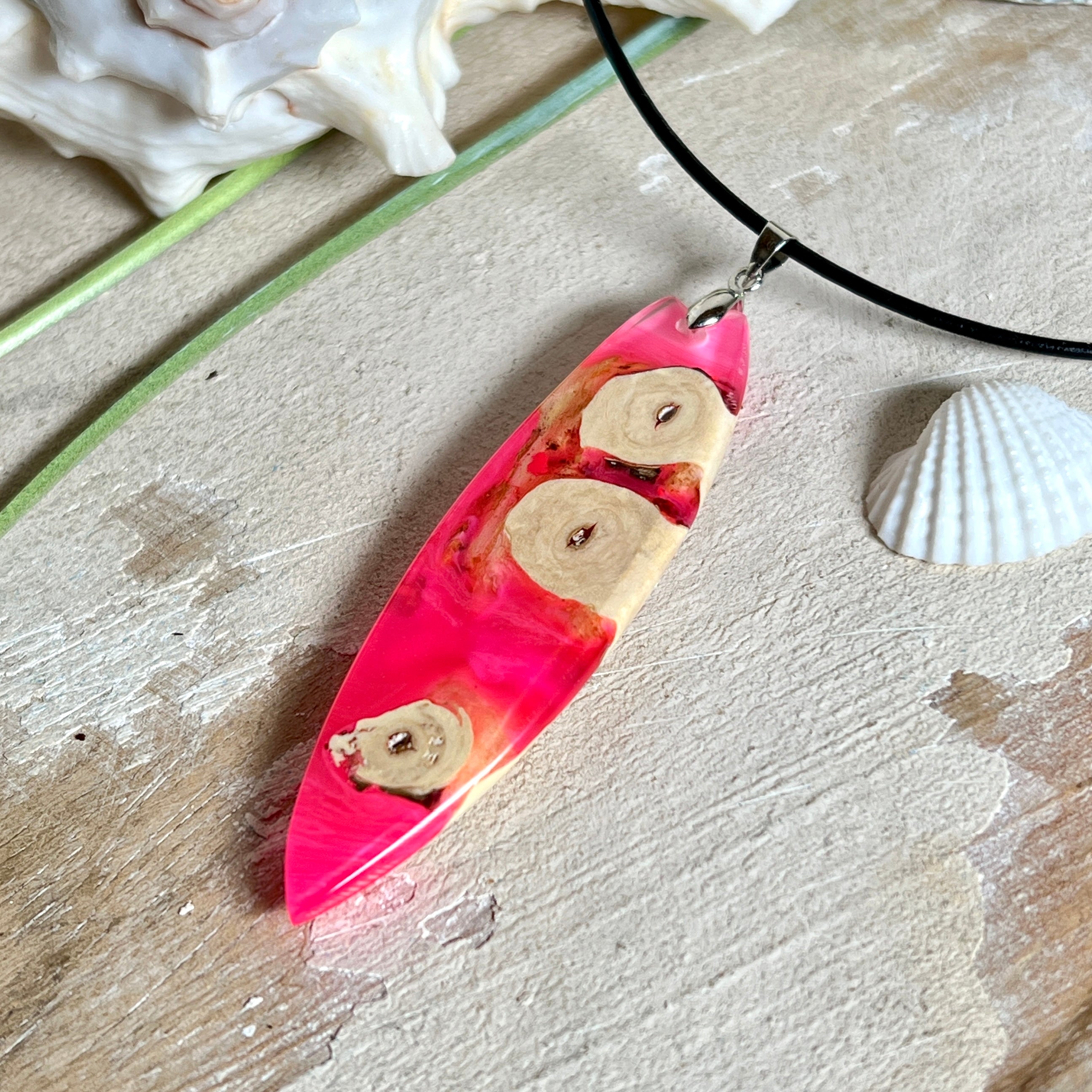 Handgefertigter Surfbrett-Anhänger „Flame Surf“ aus Maserholz und fluoreszierendem Harz in kräftigem Pink. Das Schmuckstück leuchtet bei Schwarzlicht und wird an einer schwarzen Lederkette mit Edelstahl-Karabiner (45 cm + 5 cm Verlängerung) geliefert. Größe ca. 6,7 × 2 cm. Ein Unikat für Surf- und Strandliebhaber, edel verarbeitet und mit Liebe gefertigt.