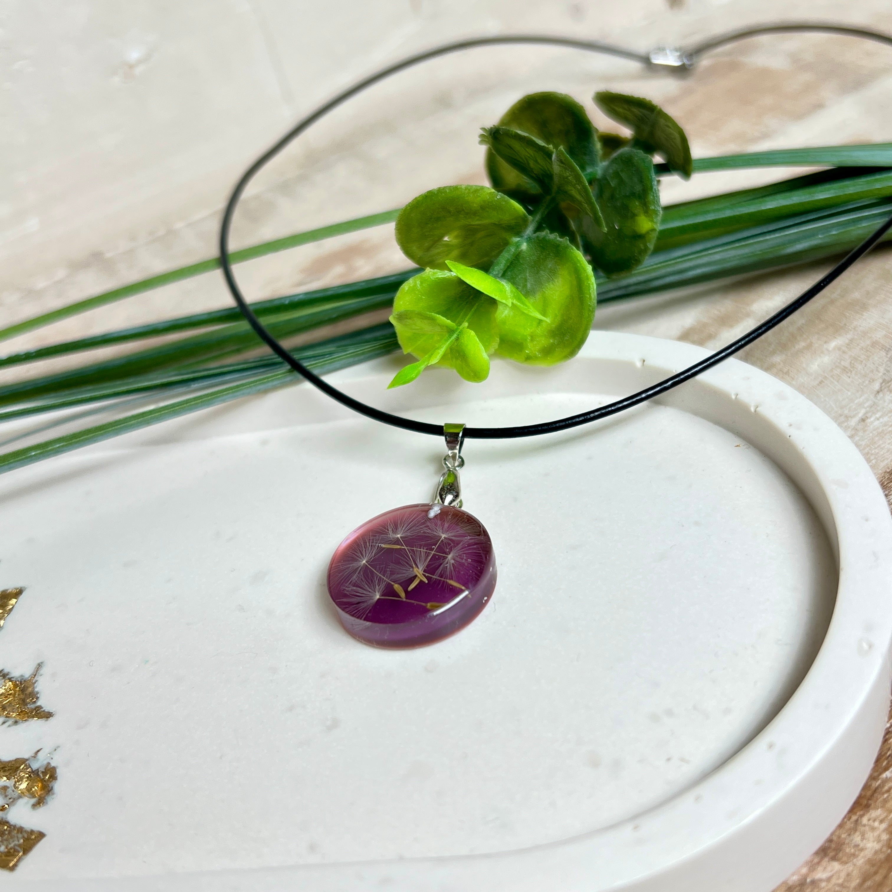 Runder Pusteblumen-Anhänger aus Harz, Hintergrund Brombeerfarben. Durchmesser 22 mm, Edelstahlöse, Lederkette verstellbar mit Edelstahlverschluss.