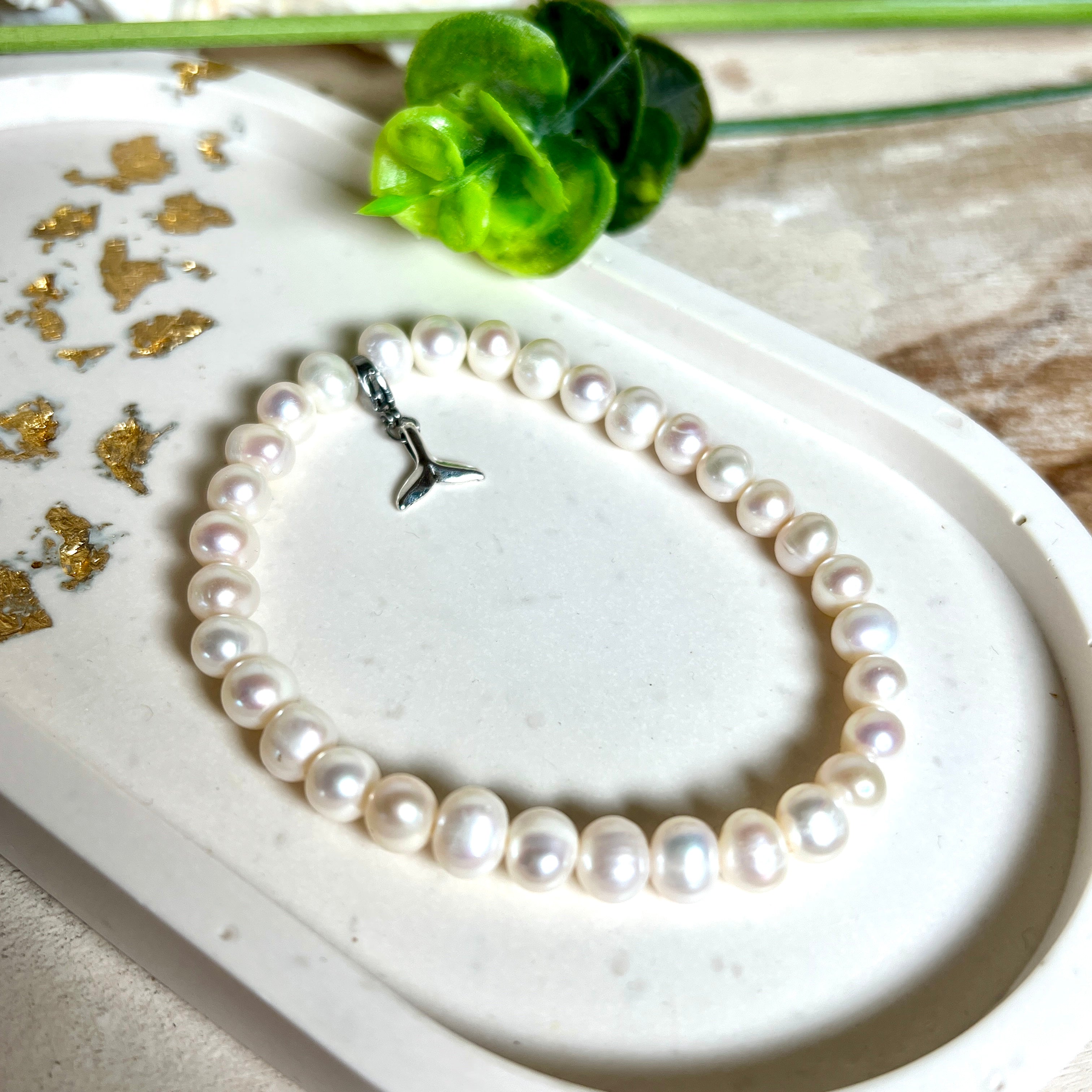 Handgefertigtes Armband aus echten Süßwasserperlen (ca. 6-7 mm), elastisch aufgezogen mit einem Edelstahl-Charm in Form einer Walflosse. Maritimes Design mit Bedeutung – stilvoll, natürlich und elegant. Größe ca. 17,5 cm. Ideal als Geschenk für Meeresliebhaberinnen oder für sich selbst.