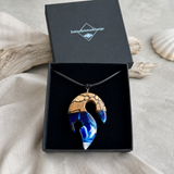 Schmuckbox-Bild TIDE – handgefertigter Holz-Harz-Anhänger aus Buchenholz und blau-weißem Epoxidharz in Maori-Angelhaken-Form, am schwarzen Lederband in schwarzer Schmuckbox von ZeitlosSchmuckDesign präsentiert.