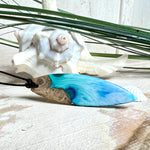 Surfbrett-Anhänger handgefertigt aus Maserholz & Harz in Blau-Weiß. Größe ca. 6,3 × 2 cm. Lederband verstellbar 26–47 cm, Schiebeknoten mit Holzperlen.